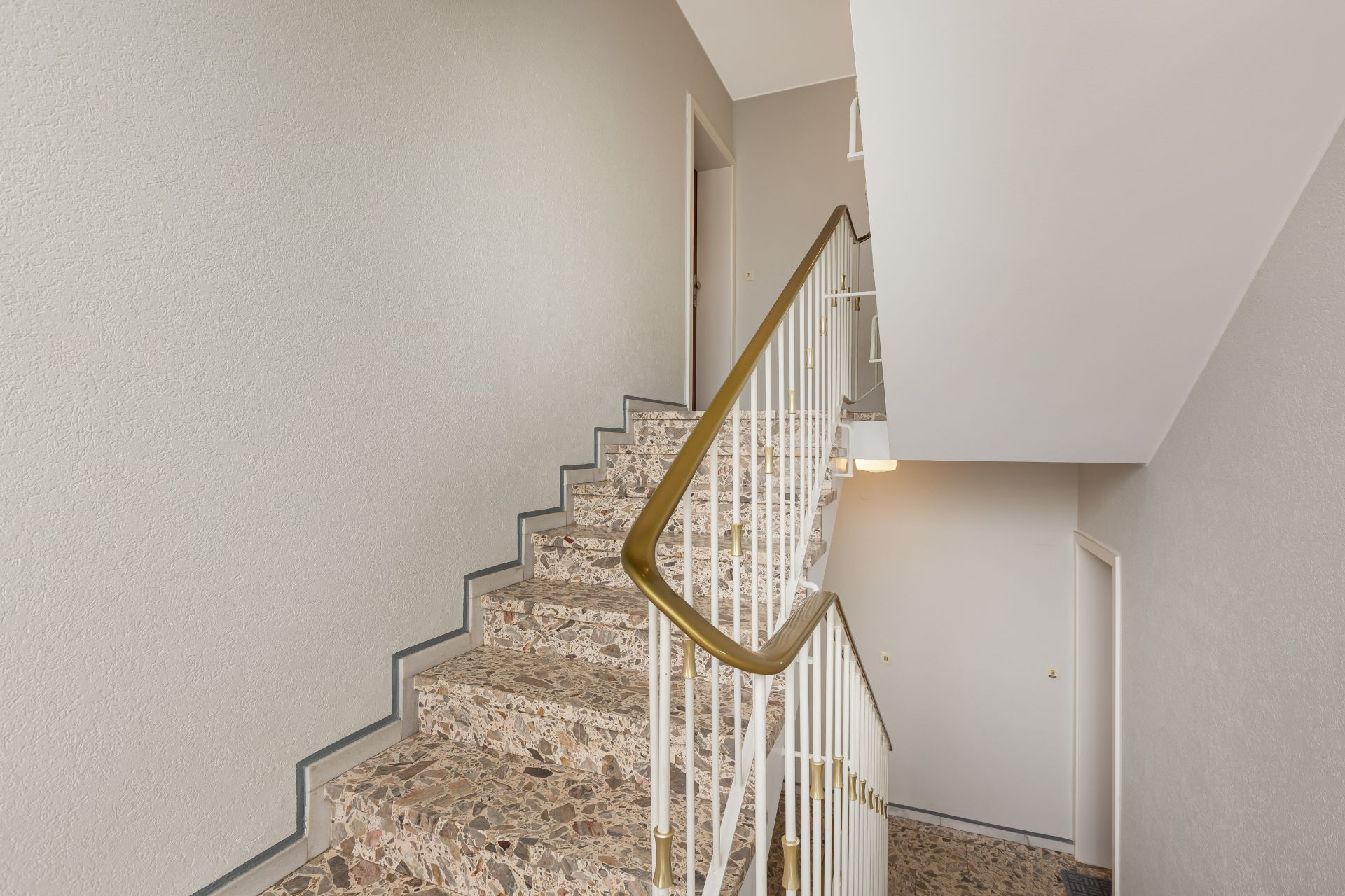 Innenansicht eines Treppenhauses mit Marmortreppe und weißem Geländer.