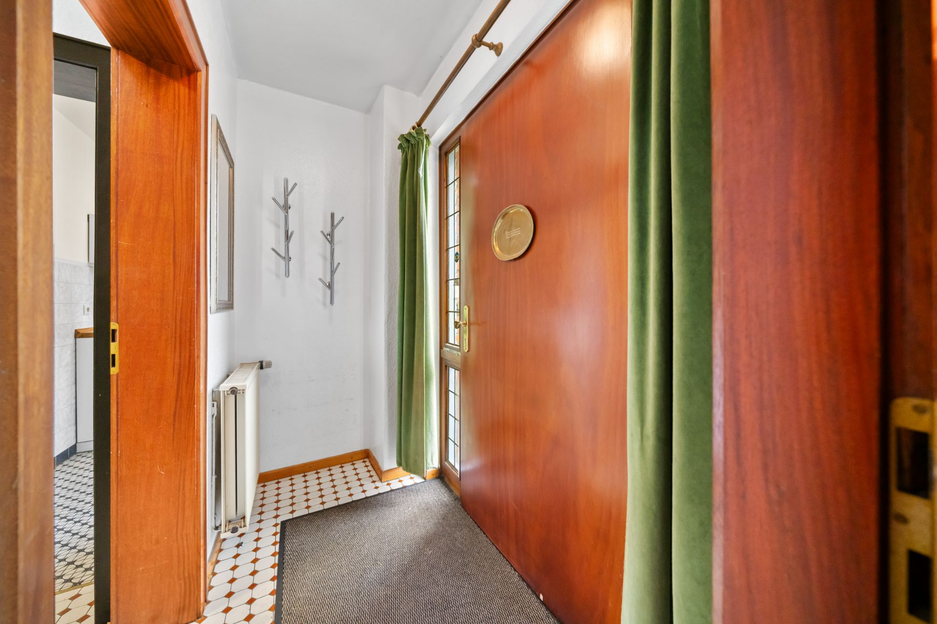 Eingangsbereich mit Holztür, grünem Vorhang, Kachelboden und Garderobenhaken an der Wand.