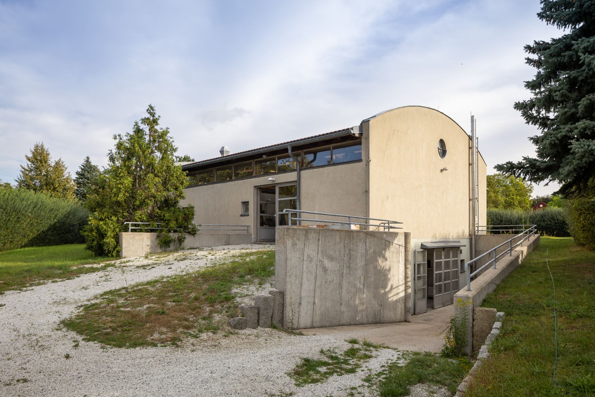 Modernes Wohnhaus mit Flachdach, Rampe und viel Grün rundherum.