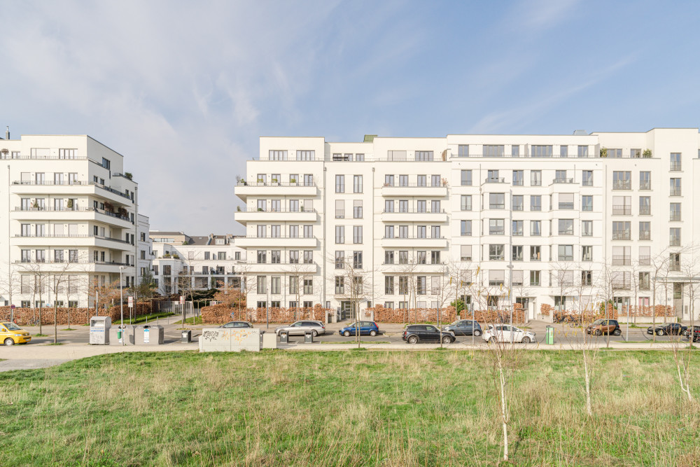 Moderne mehrstöckige Wohngebäude mit Balkonen, davor Straße und Grünfläche.