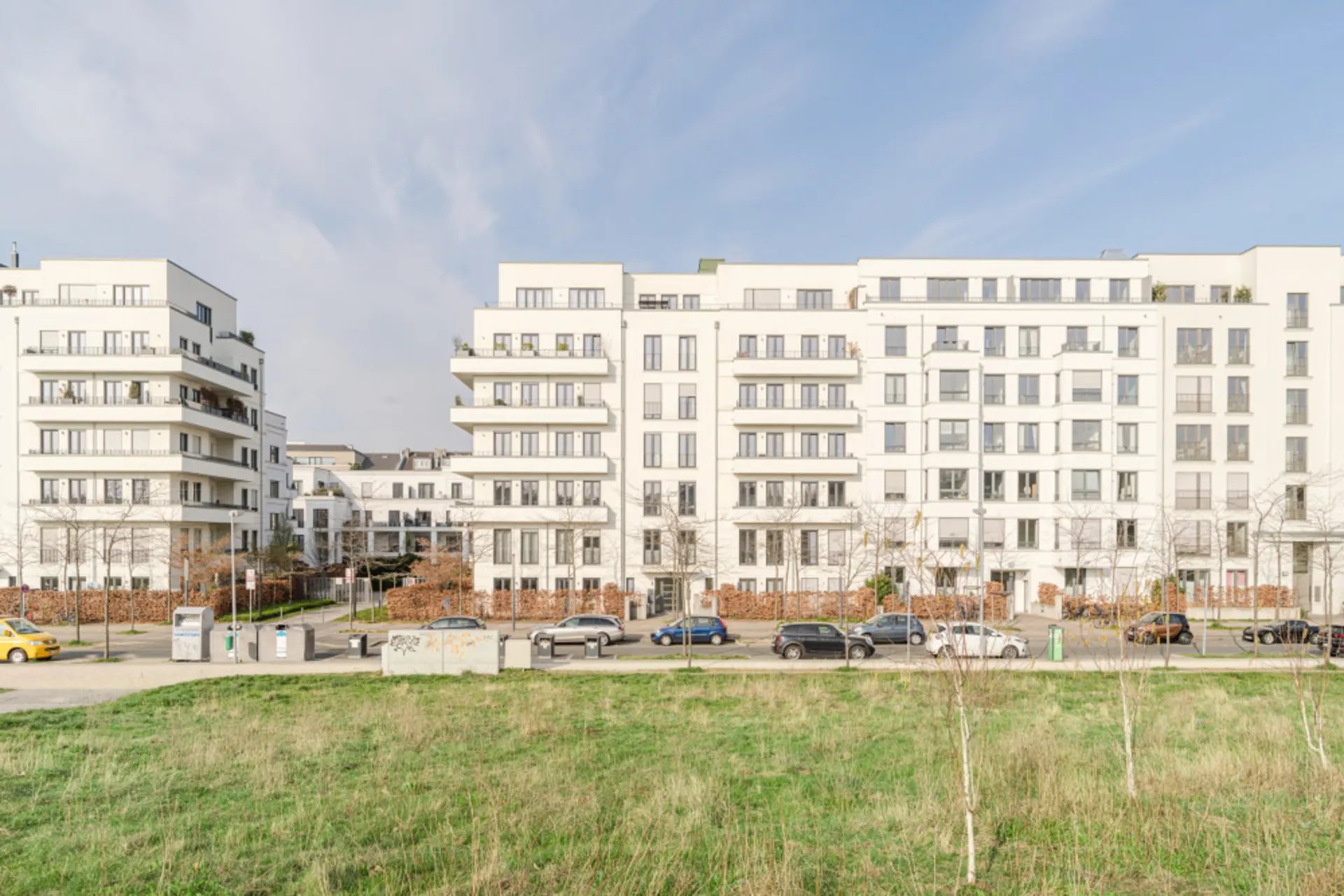 Moderne mehrstöckige Wohngebäude mit Balkonen, davor Straße und Grünfläche.