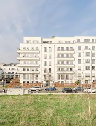 Moderne mehrstöckige Wohngebäude mit Balkonen, davor Straße und Grünfläche.