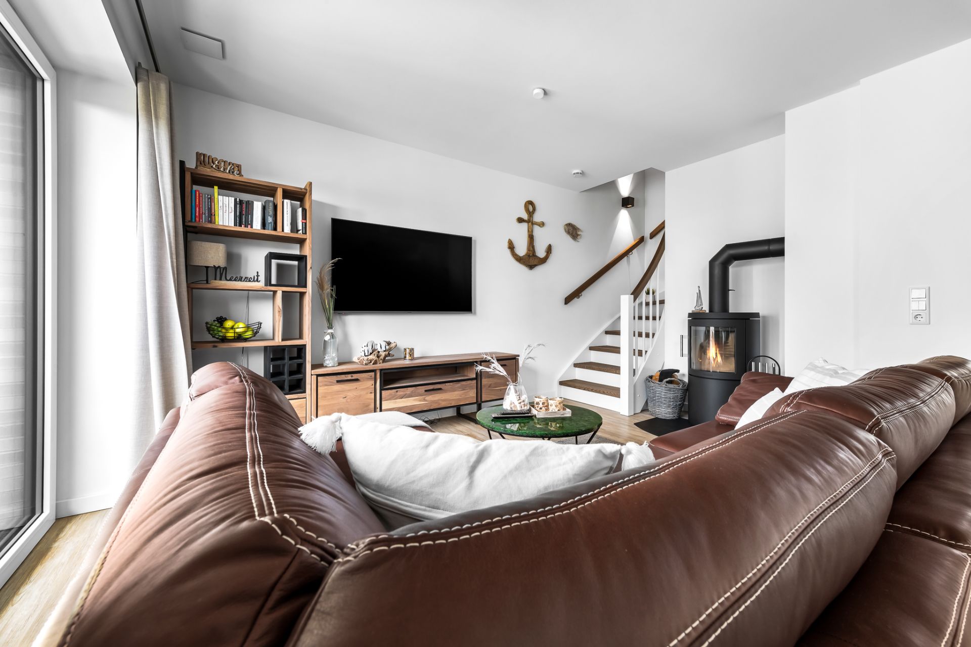 Modernes Wohnzimmer mit braunem Ledersofa, Kamin, Regal, Fernseher und Treppe.