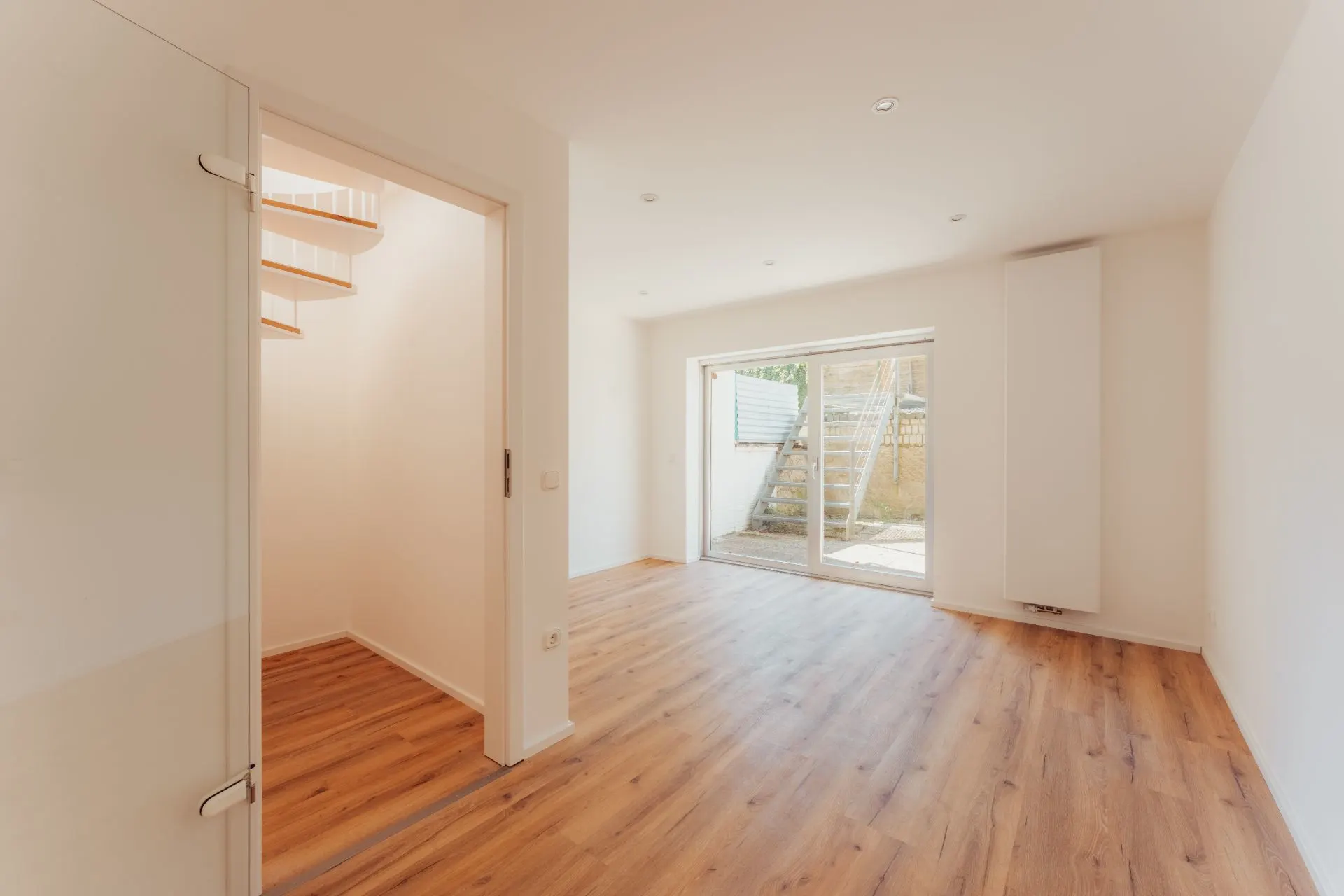 Helles Wohnzimmer mit Holzfußboden, Glastür, Treppe und Zugang zur Terrasse mit Außentreppe.