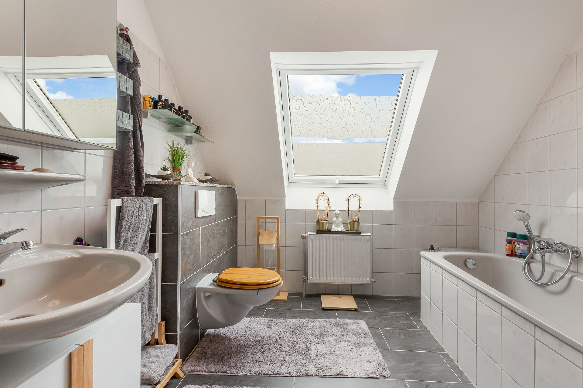 Modernes Badezimmer mit Dachfenster, Badewanne, WC, Waschbecken und grauen Fliesen.
