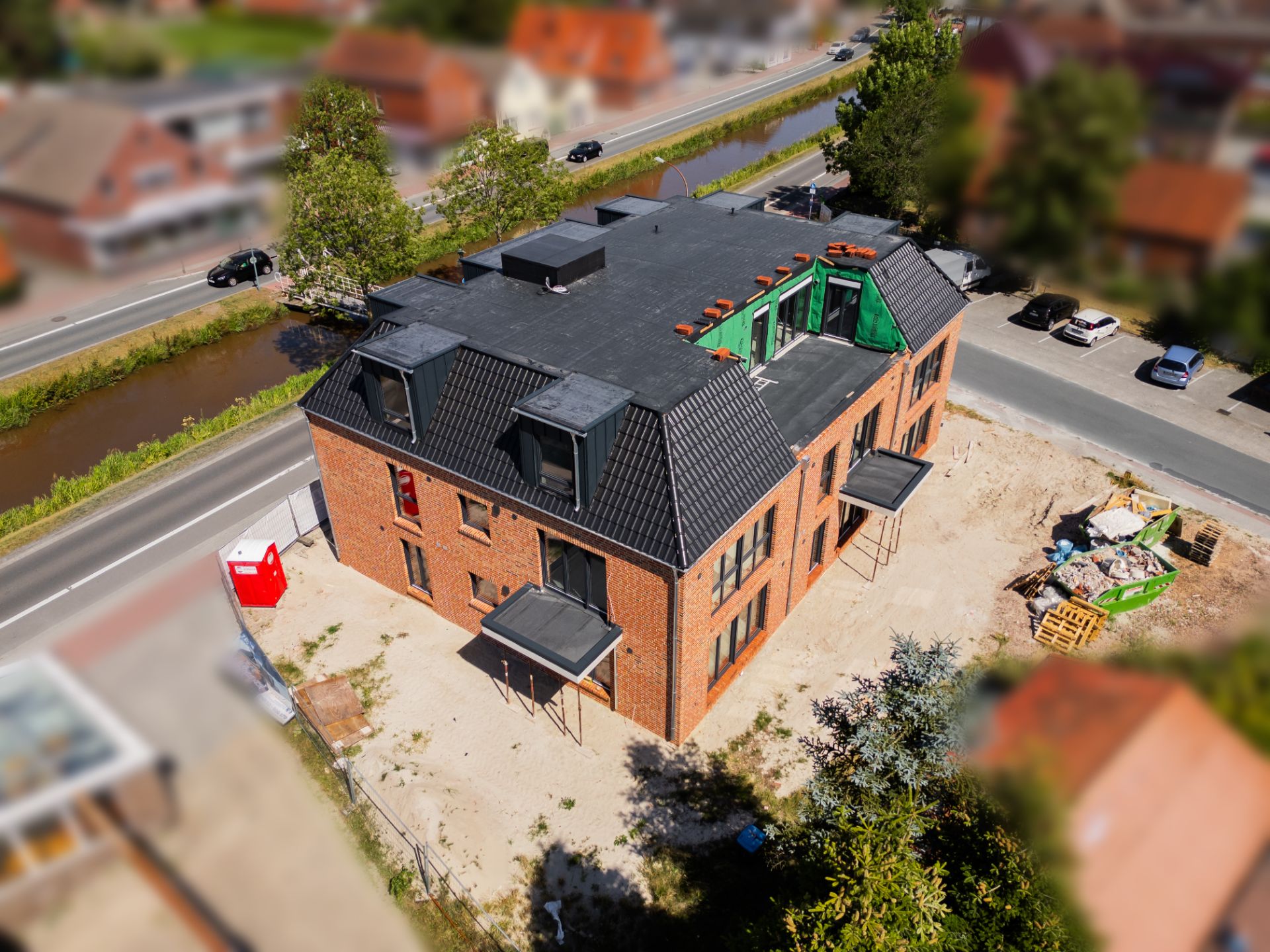 Neubau eines mehrstöckigen Wohnhauses aus Backstein mit Flachdach und Baustelle davor.