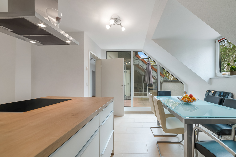 Moderne Küche mit Kochinsel, Esstisch und Stühlen neben großen Fenstern und Tür zur Terrasse.