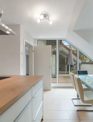 Moderne Küche mit Kochinsel, Esstisch und Stühlen neben großen Fenstern und Tür zur Terrasse.