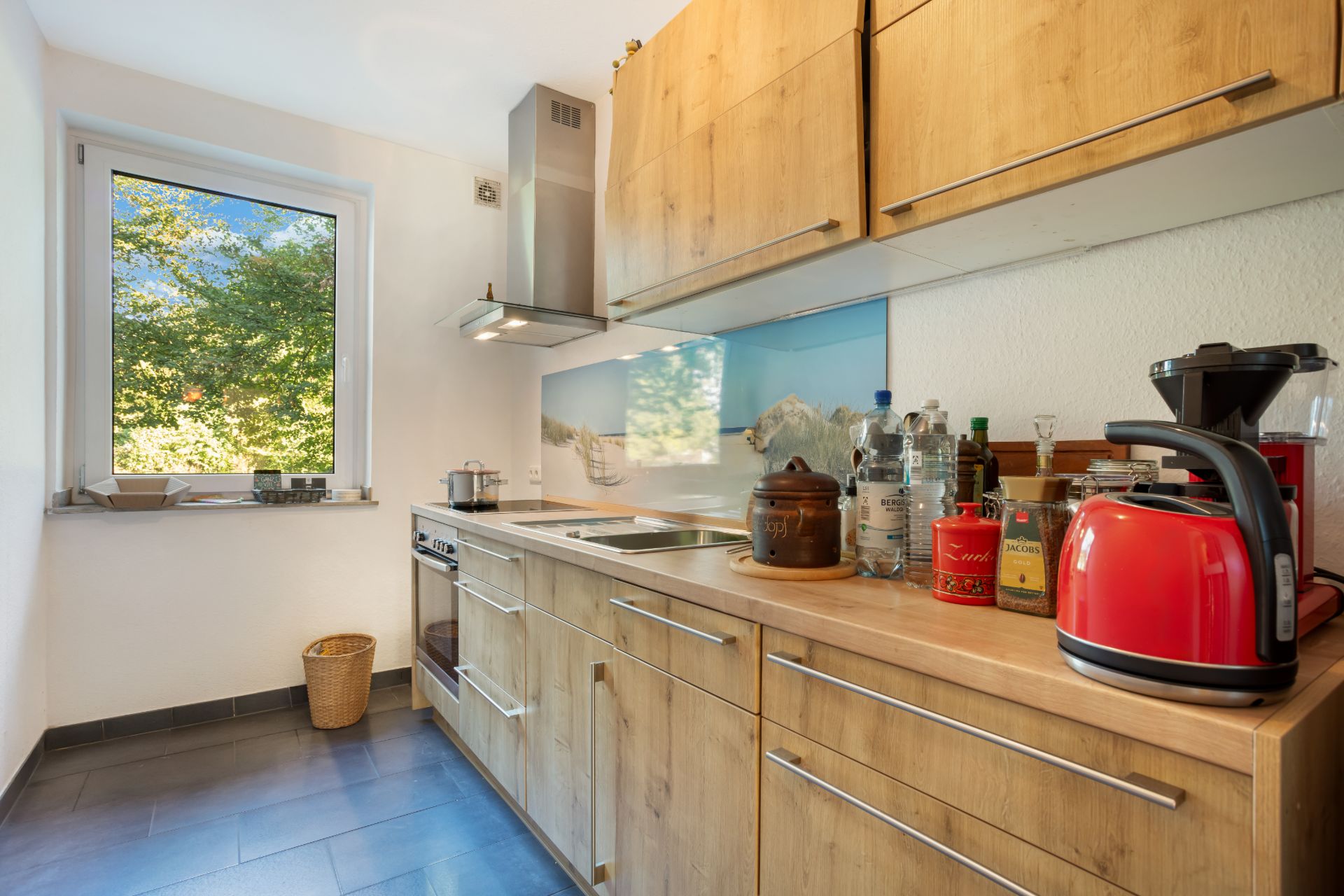 Moderne Küche mit Holzschränken, Elektrogeräten und Fenster mit Blick ins Grüne.