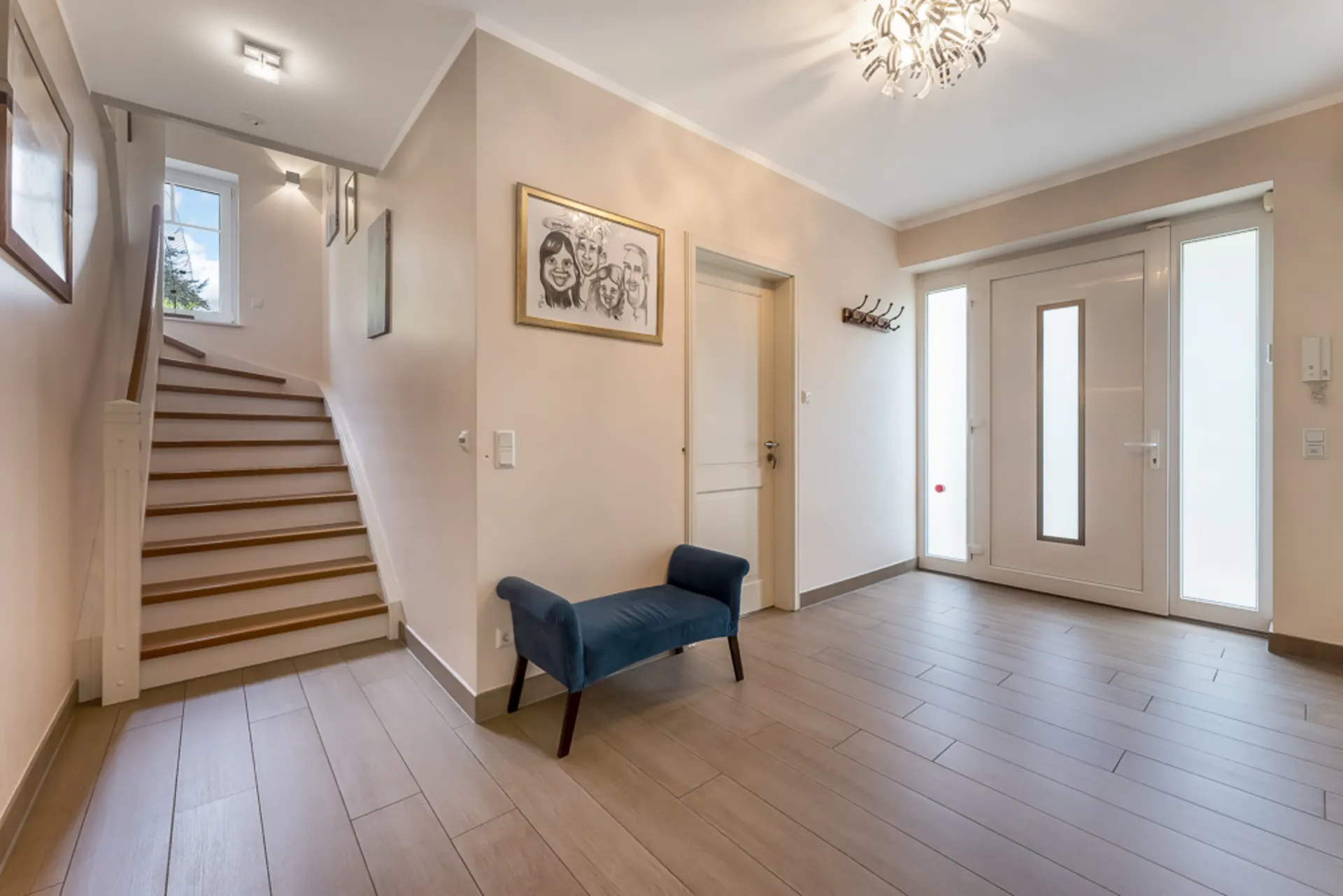 Heller Flur mit Treppe, Haustür, Bank und Wandbildern in einem Wohnhaus.