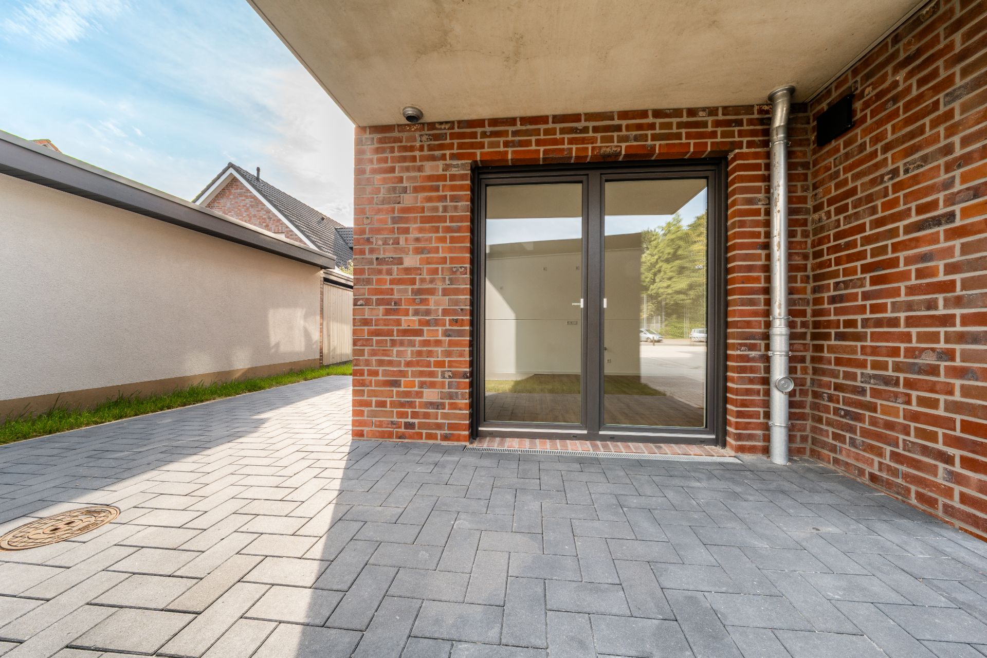 Überdachte Terrasse mit Pflastersteinen und Glastür an einem Backsteinhaus.