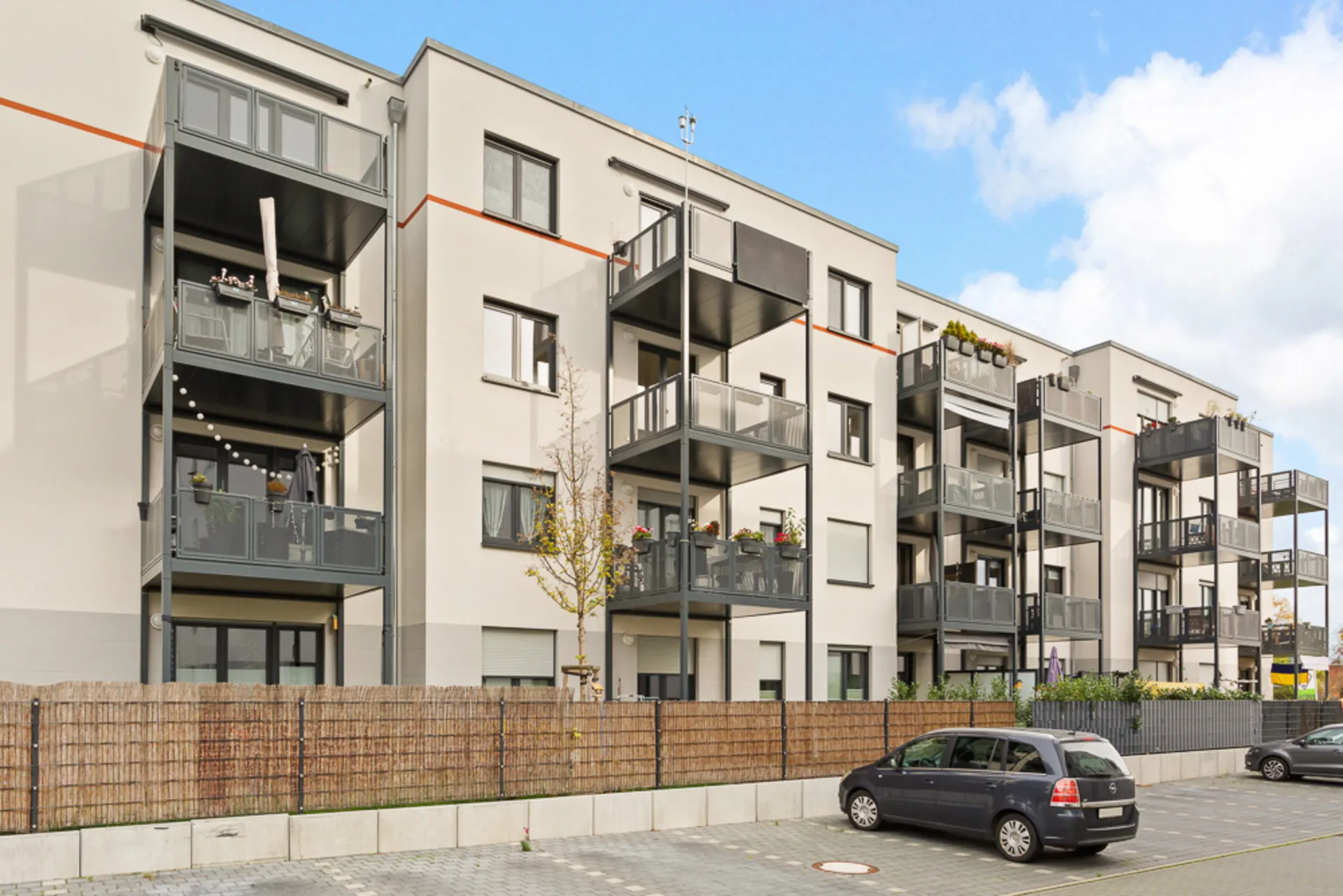 Modernes Mehrfamilienhaus mit mehreren Balkonen und geparkten Autos davor.