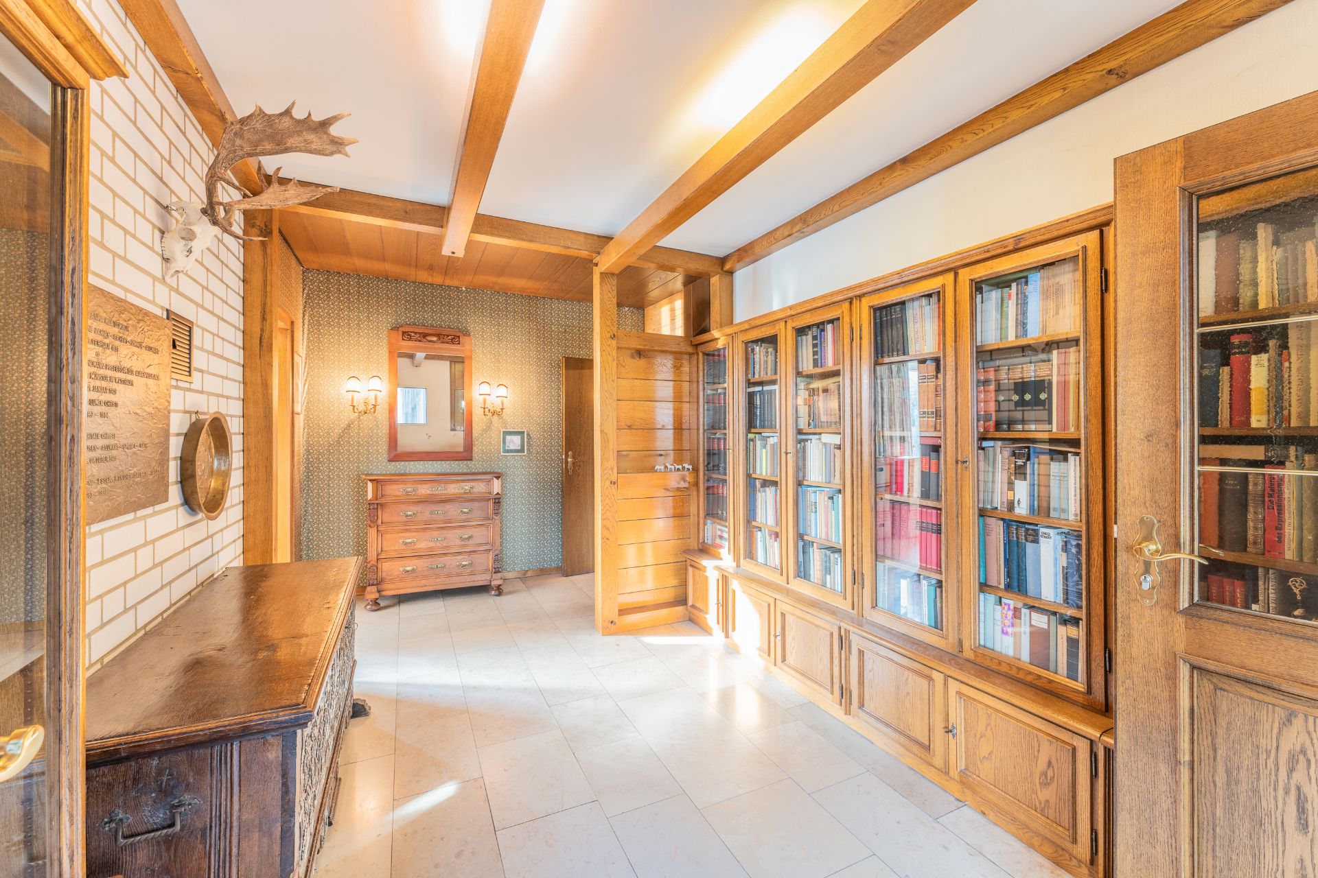 Heller Flur mit Bücherregal, Holzmöbeln, Spiegel und Wandbeleuchtung.