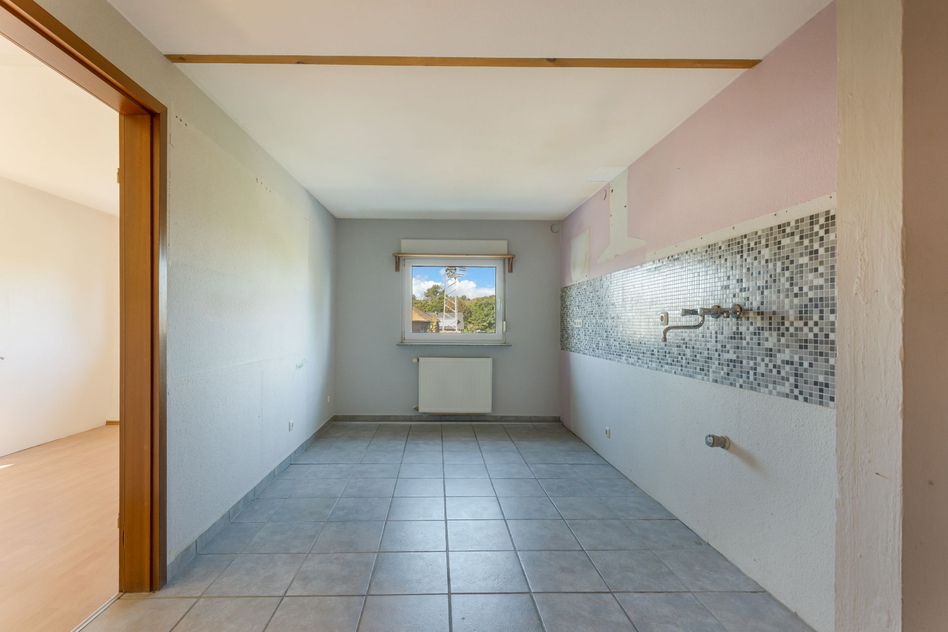 Leerer Raum mit Fliesenboden, Mosaikfliesen an der Wand und Fenster am Ende.