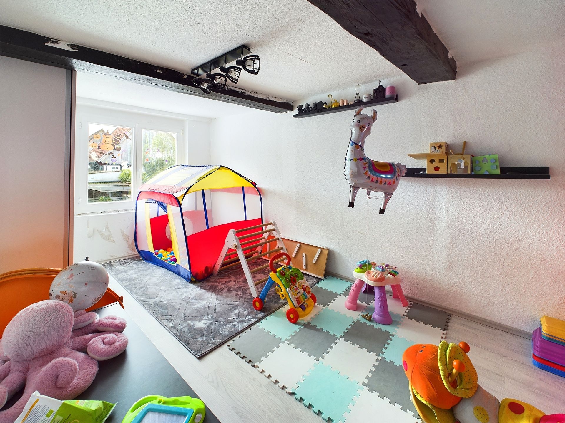 Kinderzimmer mit buntem Spielzelt, Spielzeug und Schaumstoffmatten auf dem Boden.