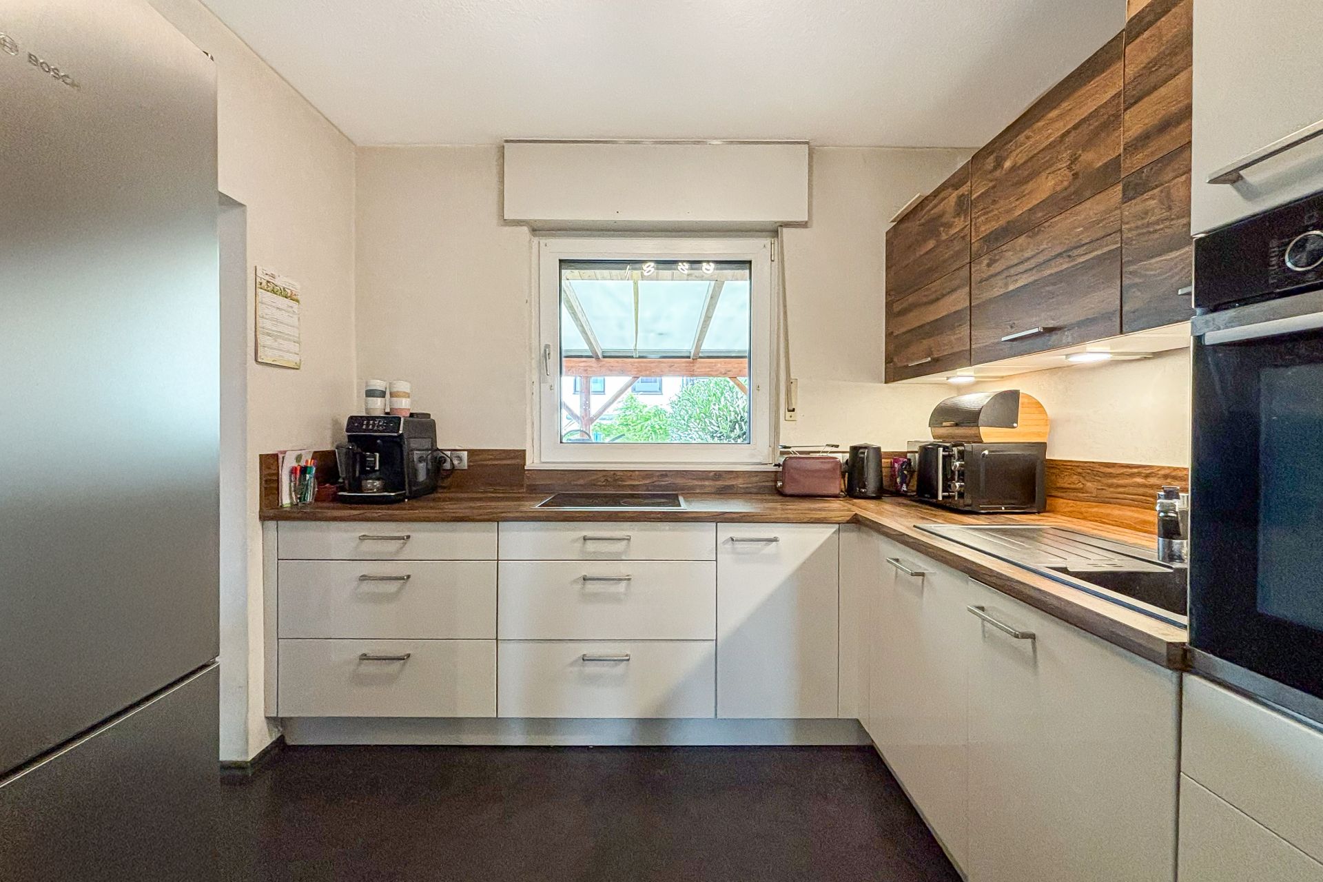 Moderne Küche mit weißen Schränken, Holzarbeitsplatte und Fensterausblick.