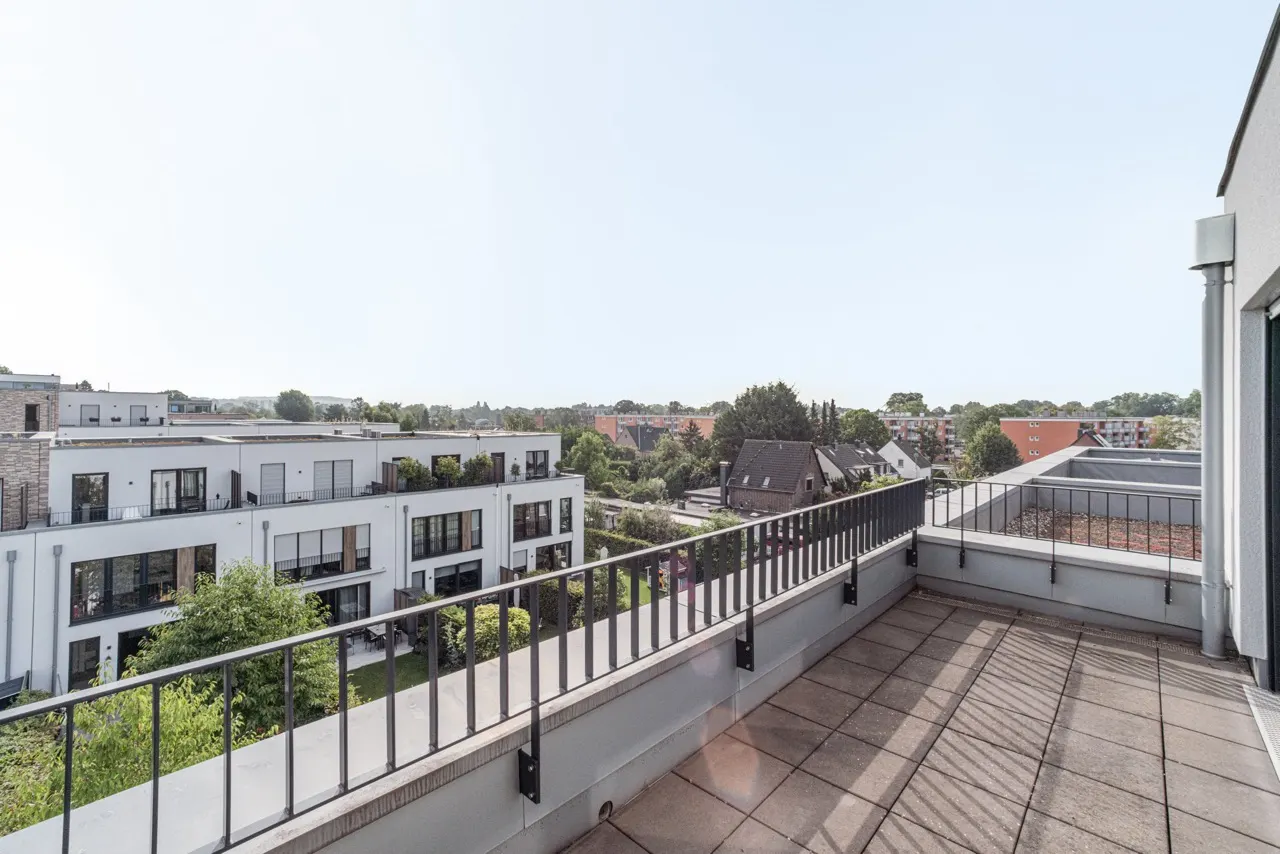 Große Dachterrasse mit Blick auf moderne Wohngebäude und grüne Umgebung.