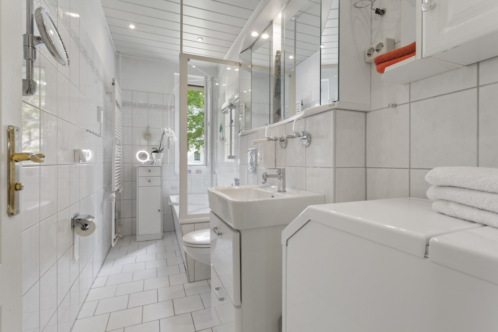 Helles, modernes Badezimmer mit Waschbecken, WC, Waschmaschine und Handtüchern.