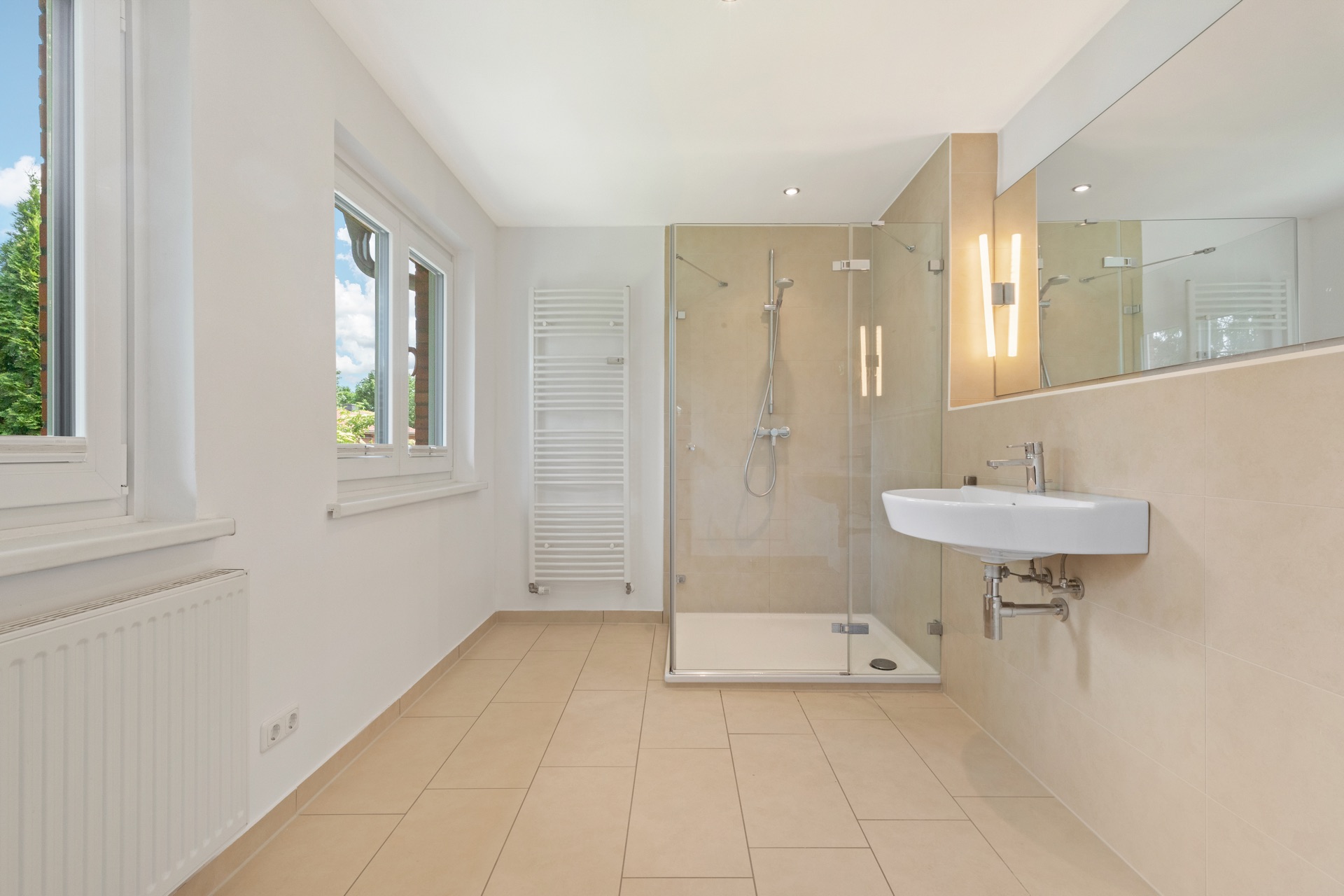Modernes Badezimmer mit Dusche, Waschbecken, großem Spiegel und zwei Fenstern.