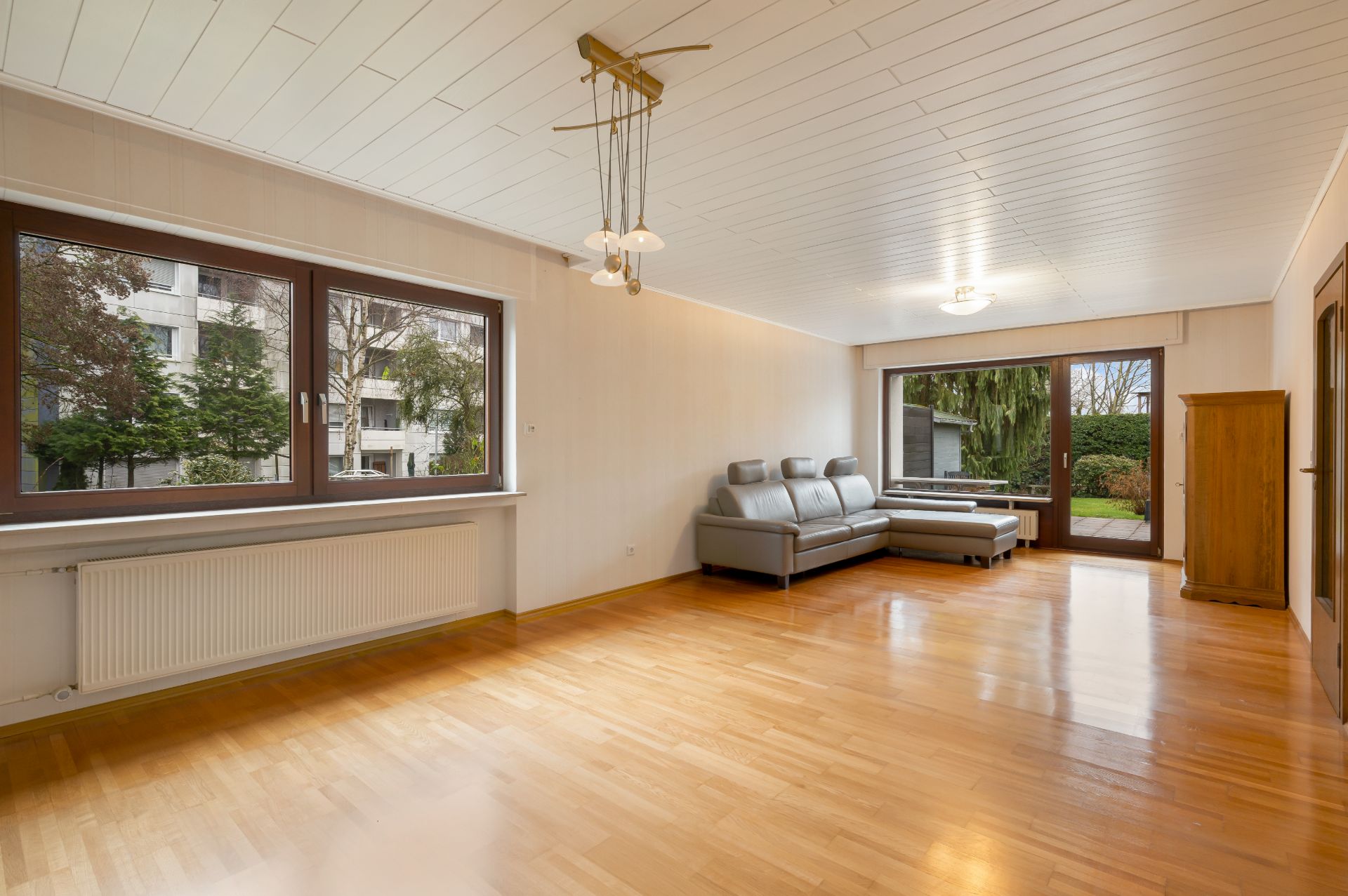 Helles Wohnzimmer mit Parkettboden, grauem Sofa, großen Fenstern und Zugang zum Garten.