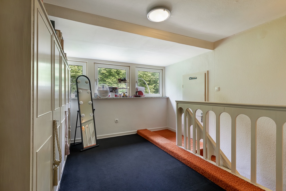 Heller Flur mit dunklem Teppich, Stehspiegel, Schrank und Fenster mit Blick ins Grüne.