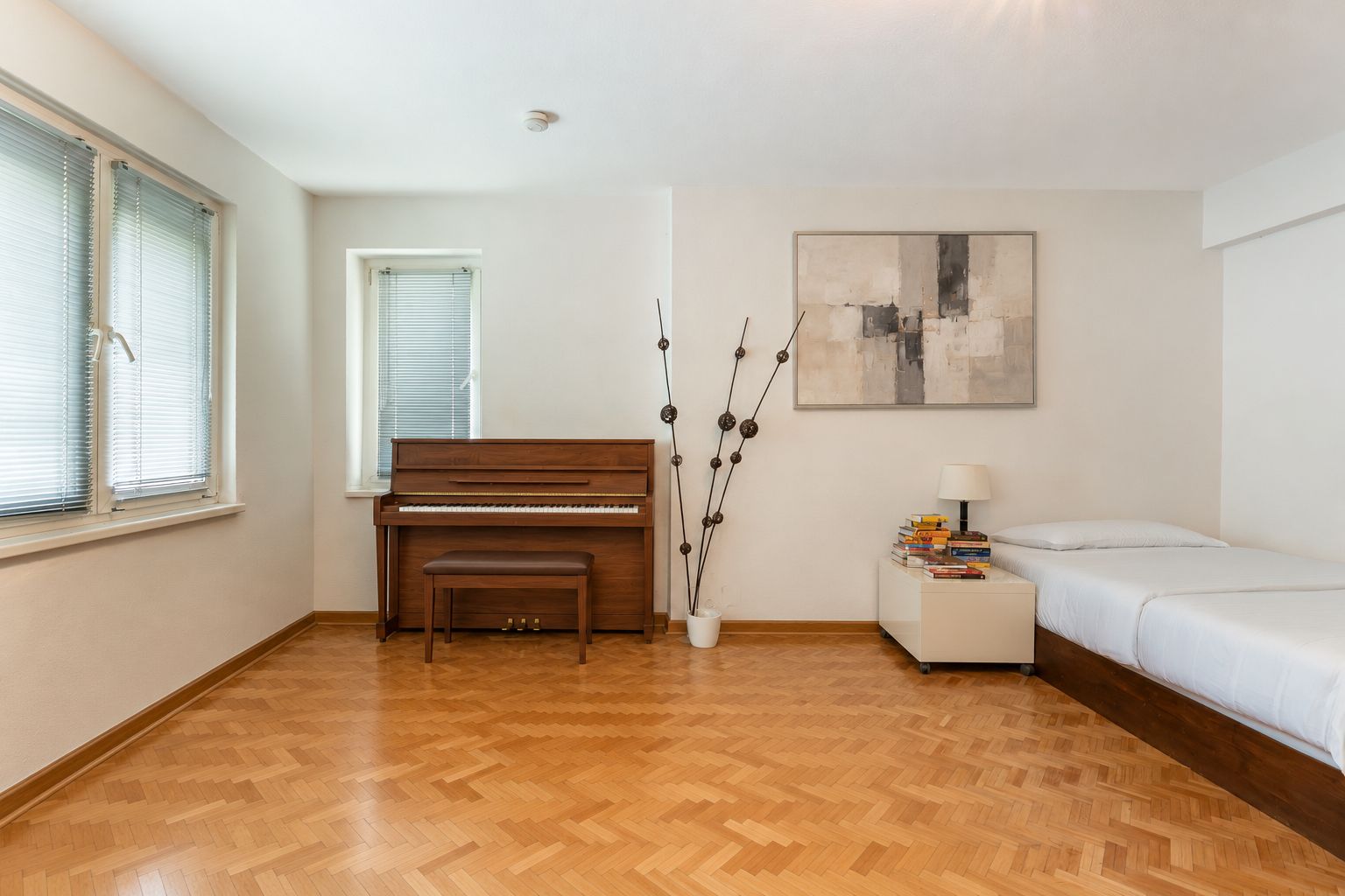 Helles Zimmer mit Klavier, Bett, Nachttisch und Kunstwerk an der Wand.