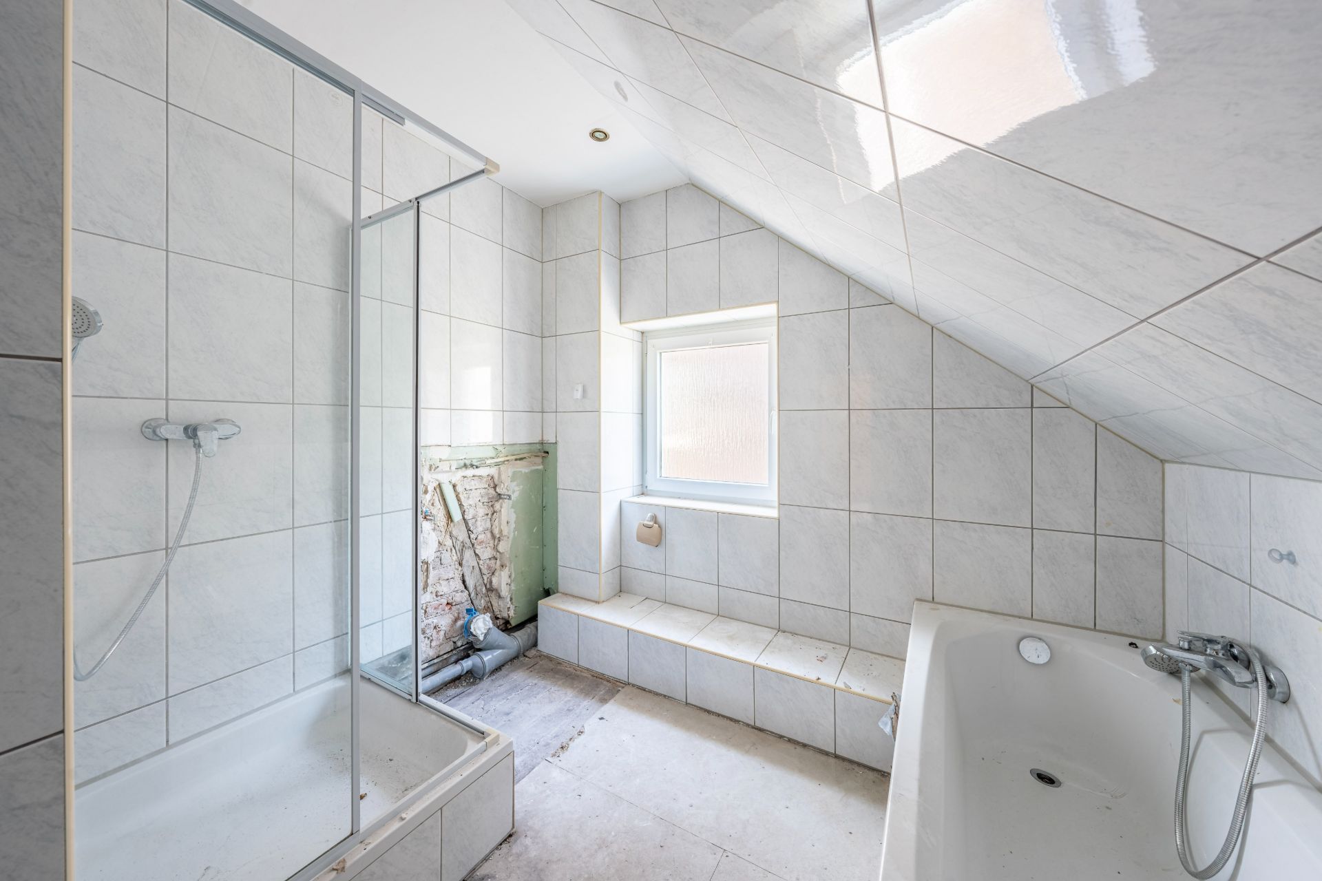 Helles Badezimmer mit Dusche, Badewanne und Fenster, teilweise nicht fertig renoviert.