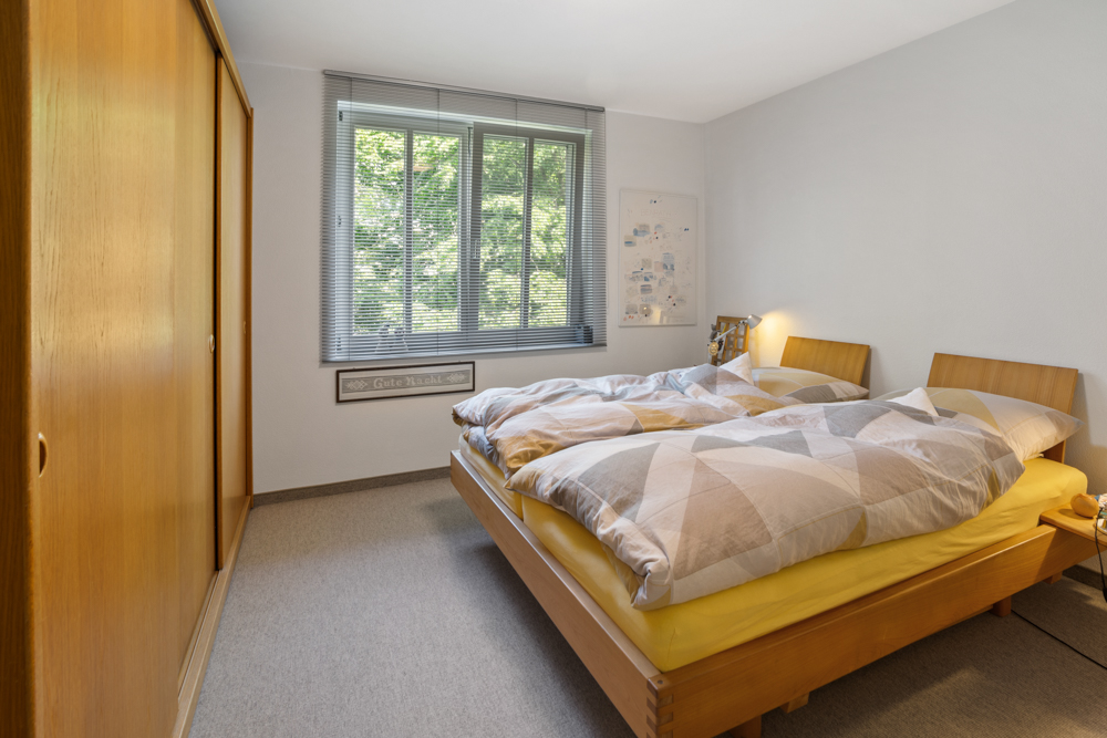 Helles Schlafzimmer mit Doppelbett, großem Holzschrank und Fenster mit Blick ins Grüne.