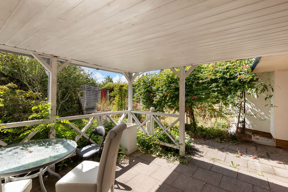 Überdachte Terrasse mit Tisch, Stühlen und Blick in einen grünen Garten.