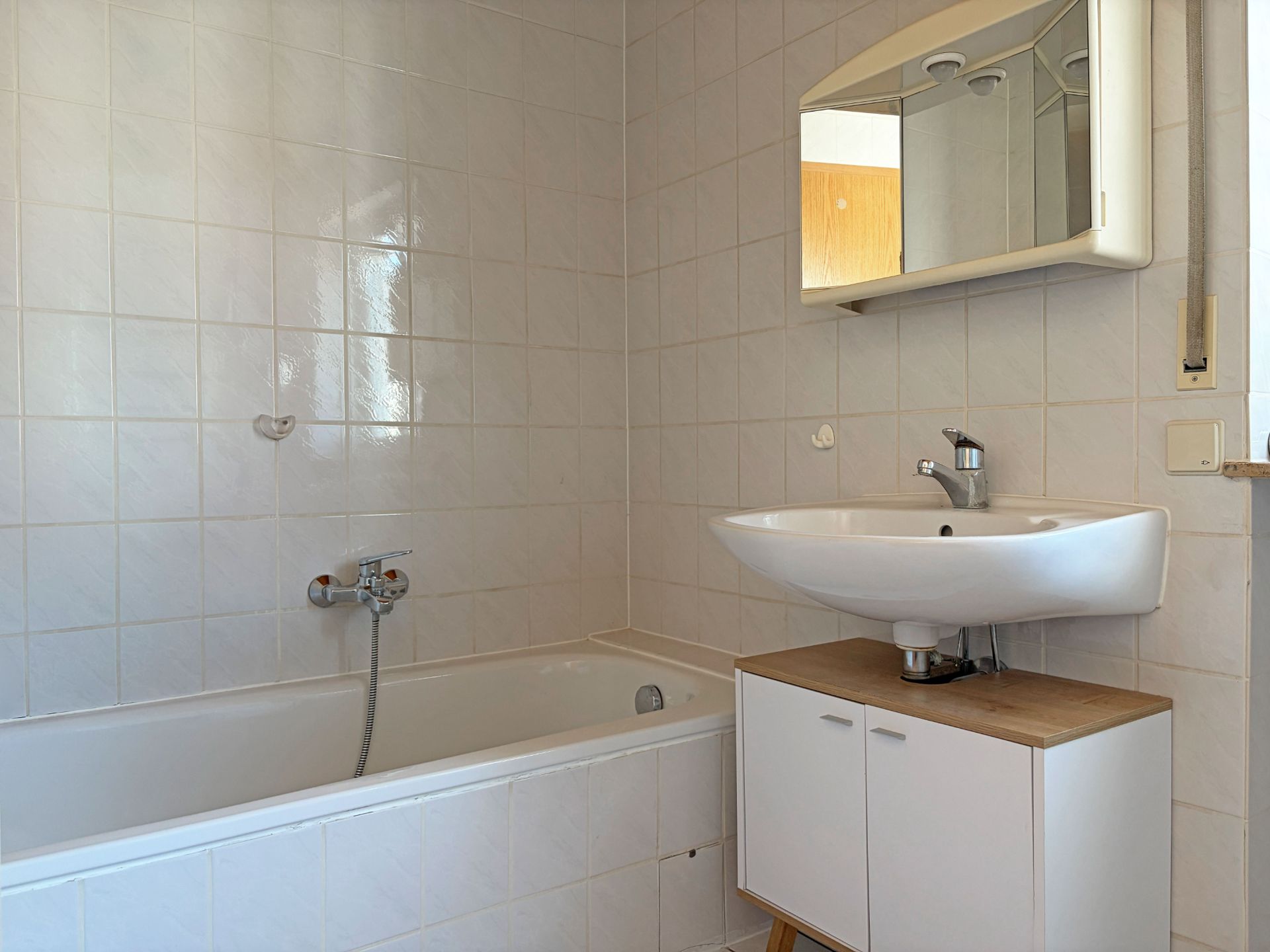 Helles Badezimmer mit Badewanne, Waschbecken, Spiegelschrank und weiß gefliesten Wänden.