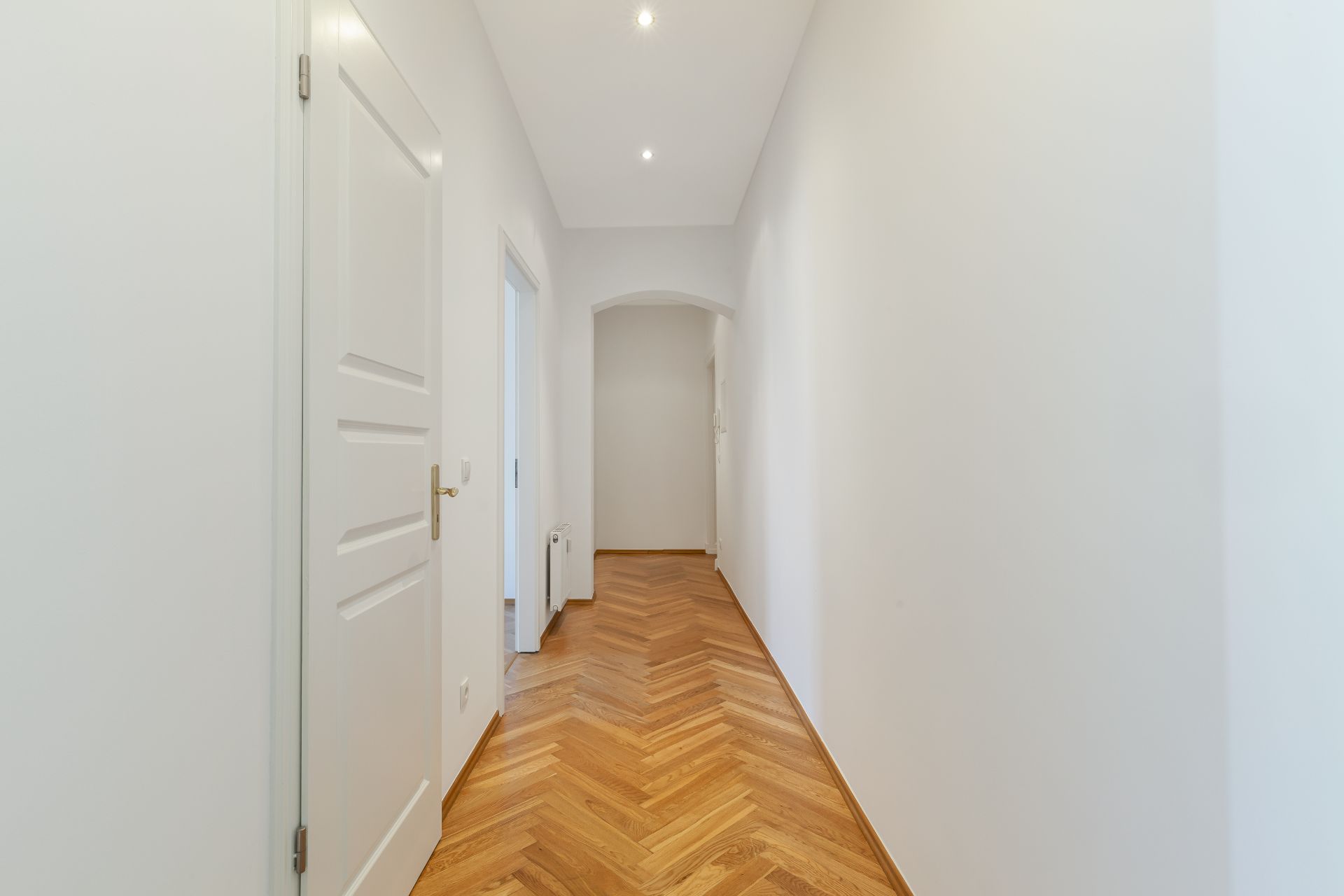 Heller Flur mit Holzboden, weißen Wänden und einer Tür links.