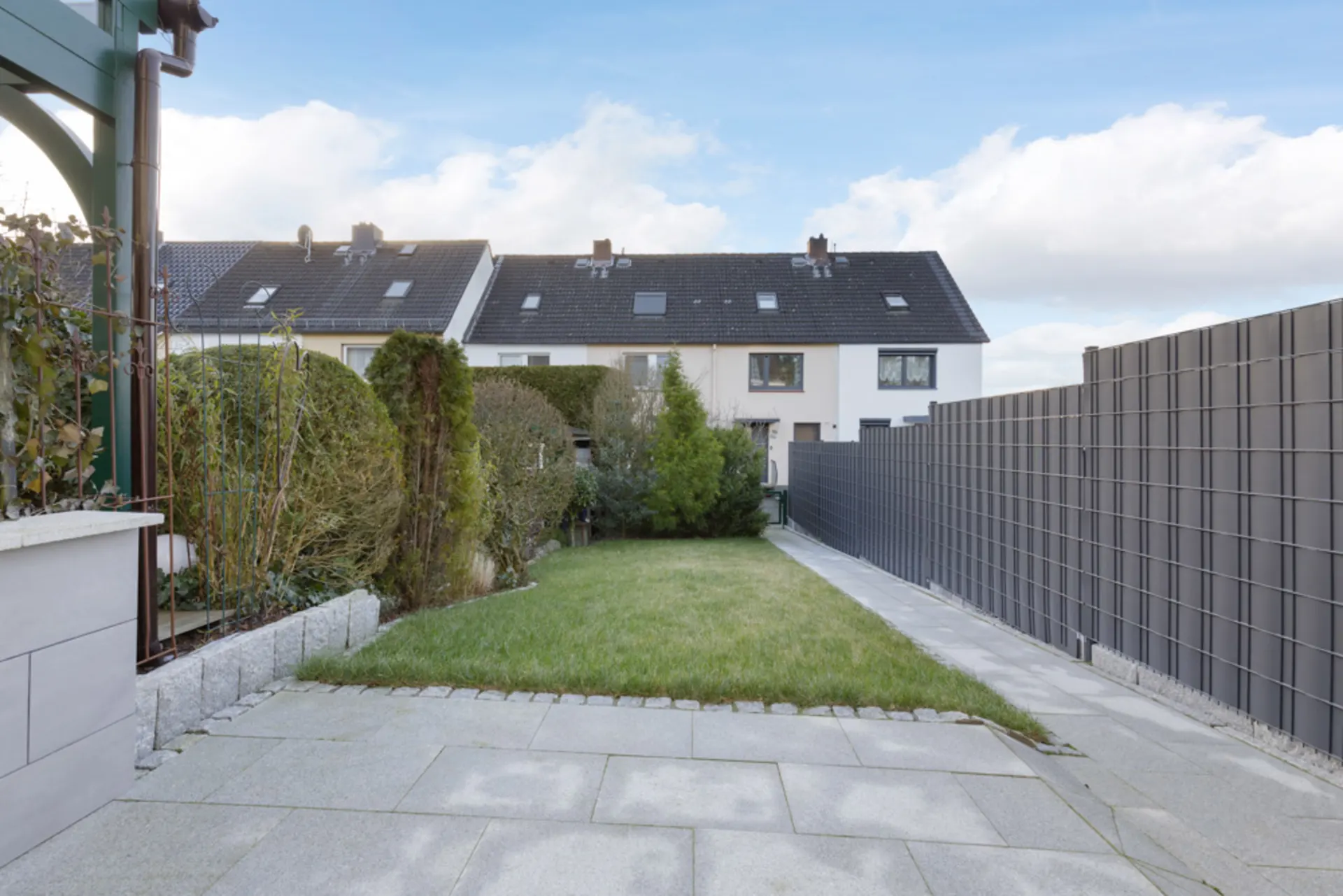 Gepflegter Garten mit Rasen, Terrasse und Sichtschutzzaun neben einem Reihenhaus.
