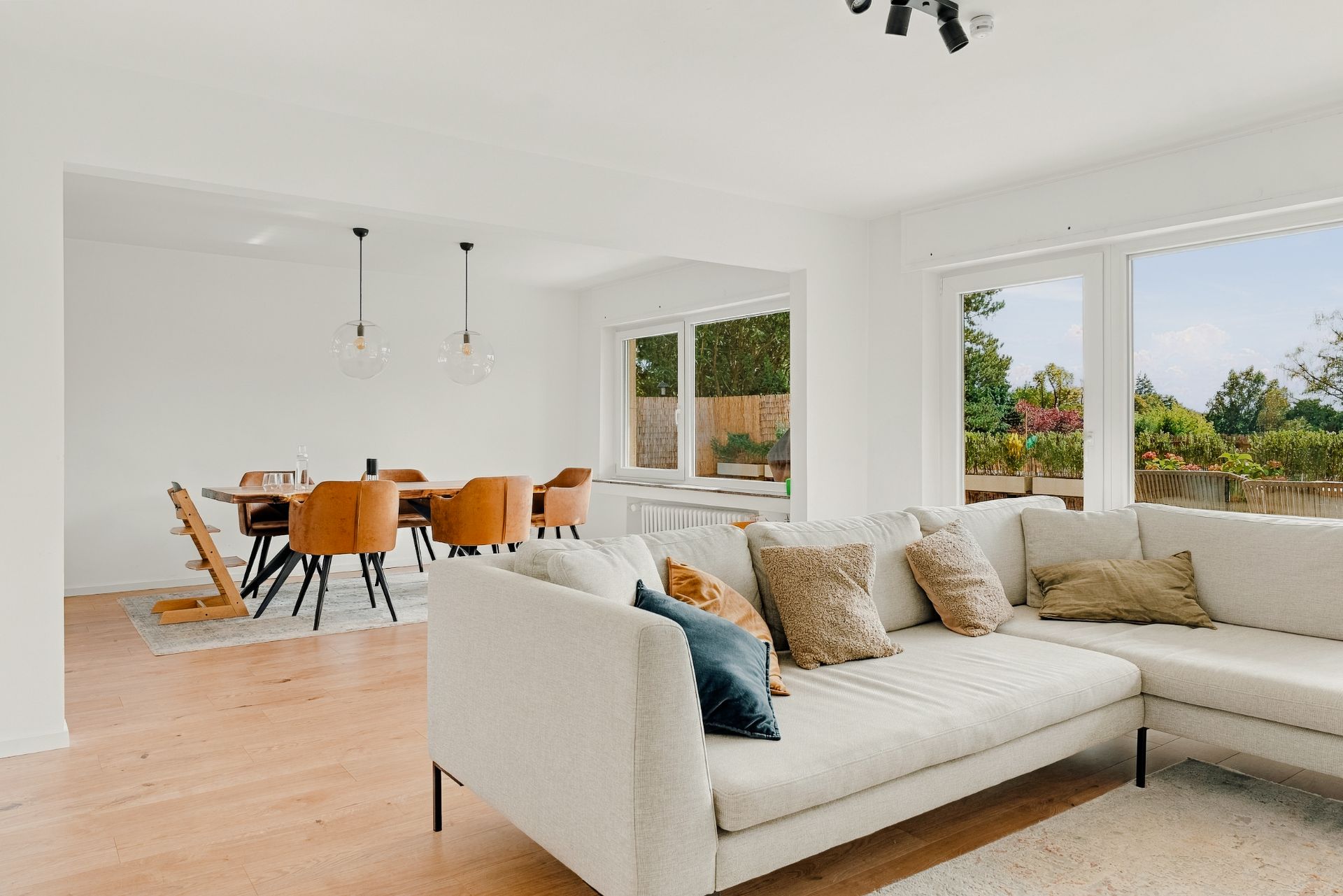 Helles Wohnzimmer mit Ecksofa, großem Fenster und angrenzendem Essbereich mit Esstisch und Stühlen.