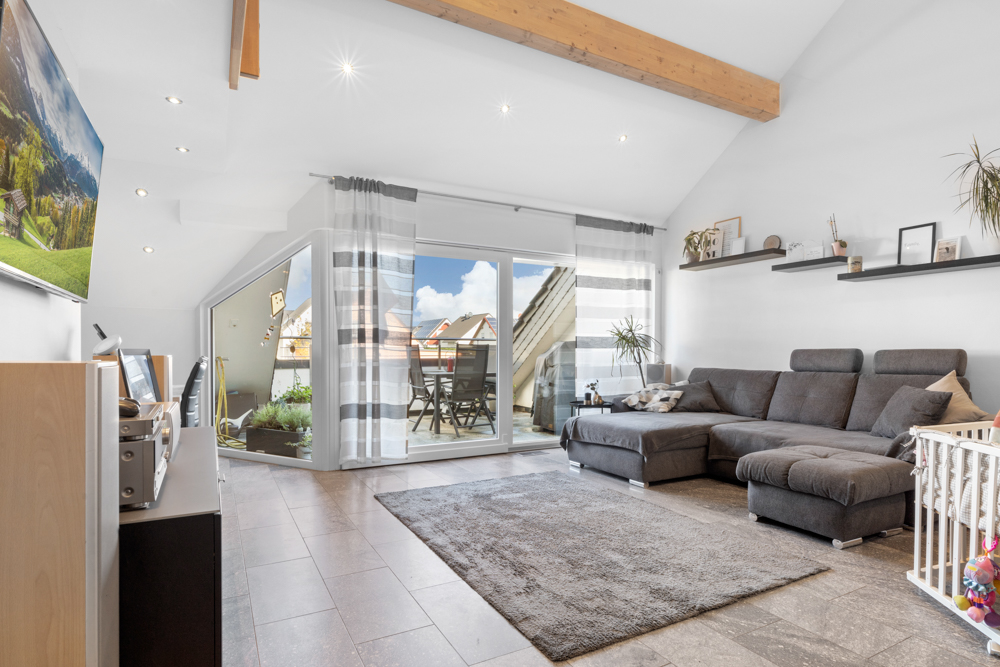 Helles Wohnzimmer mit grauem Sofa, Teppich, Schreibtisch und Zugang zum Balkon.