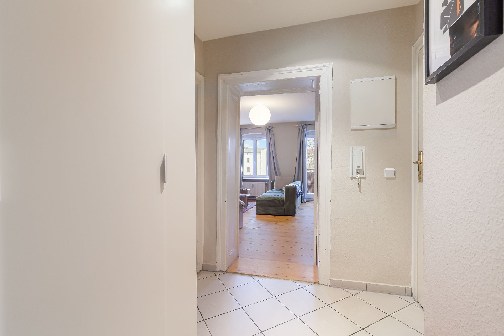Flur mit Blick in ein Wohnzimmer mit Sofa, großem Fenster und Holzboden.