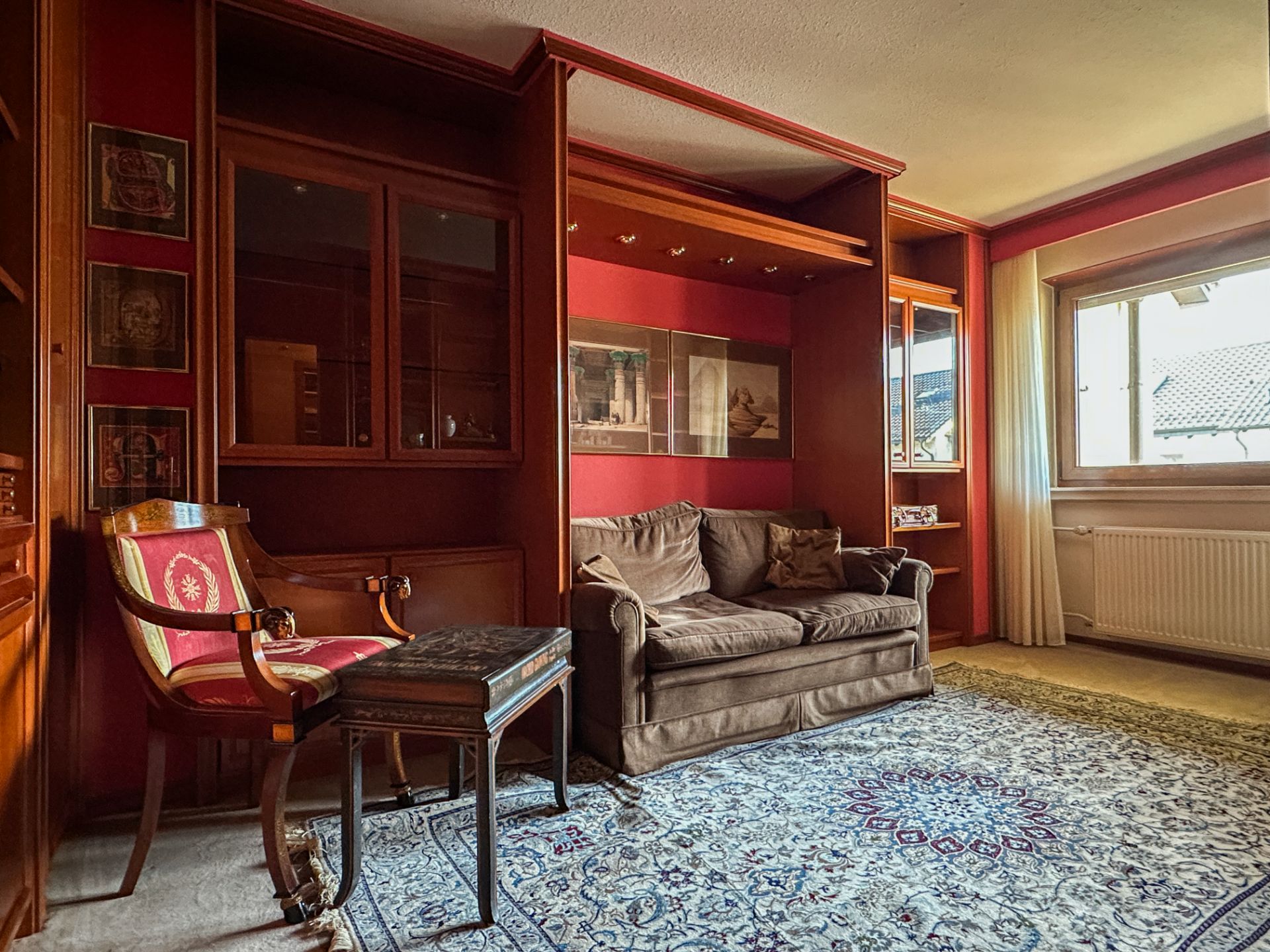 Wohnzimmer mit braunem Sofa, rotem Stuhl, Teppich und großem Fenster.