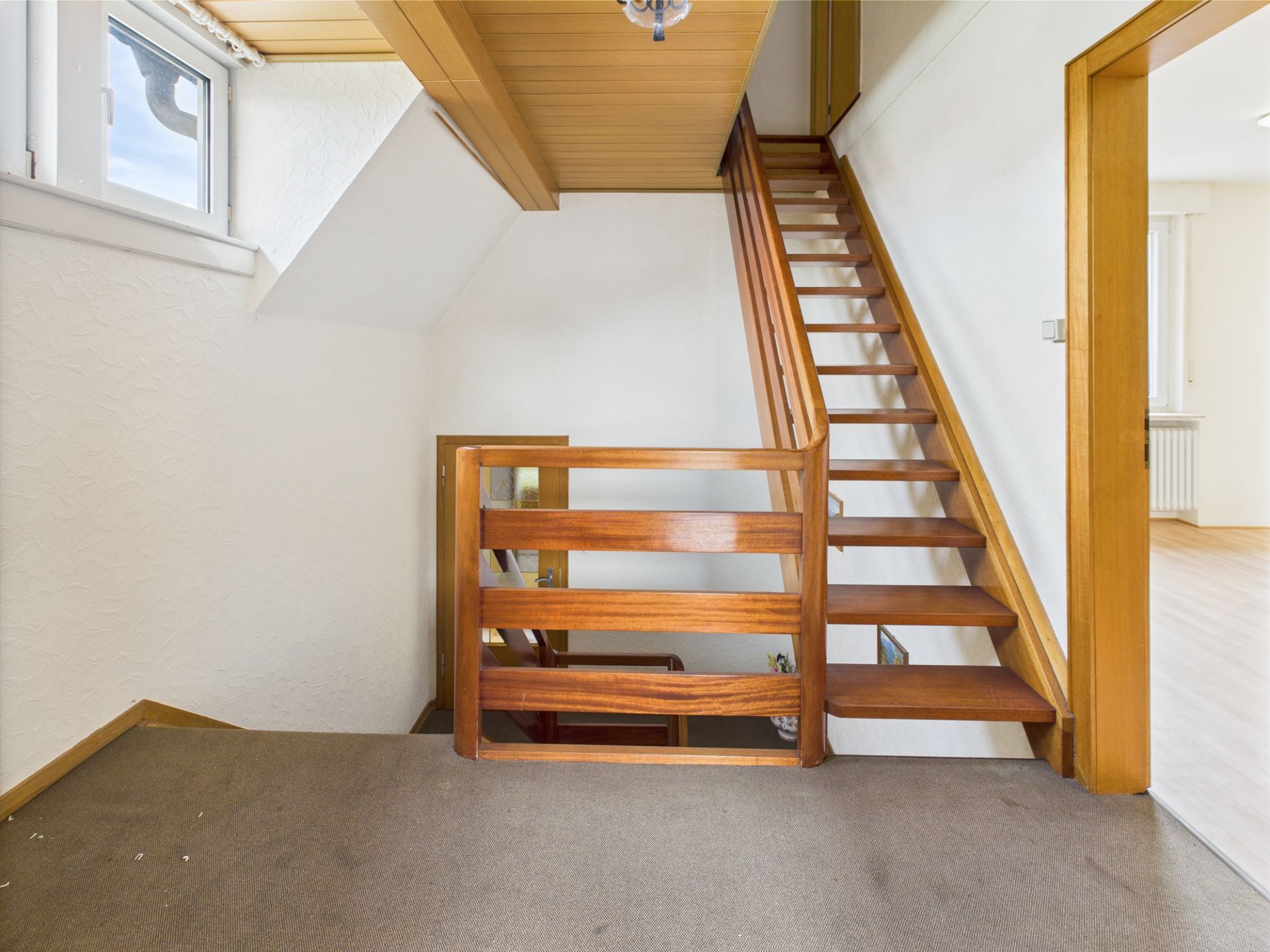Holztreppe mit Geländer und Dachfenster in einem Wohnhausflur.