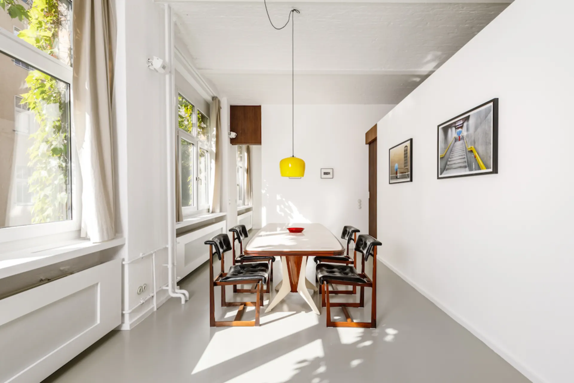 Heller Essbereich mit Holztisch, sechs Stühlen, gelber Lampe und großen Fenstern.