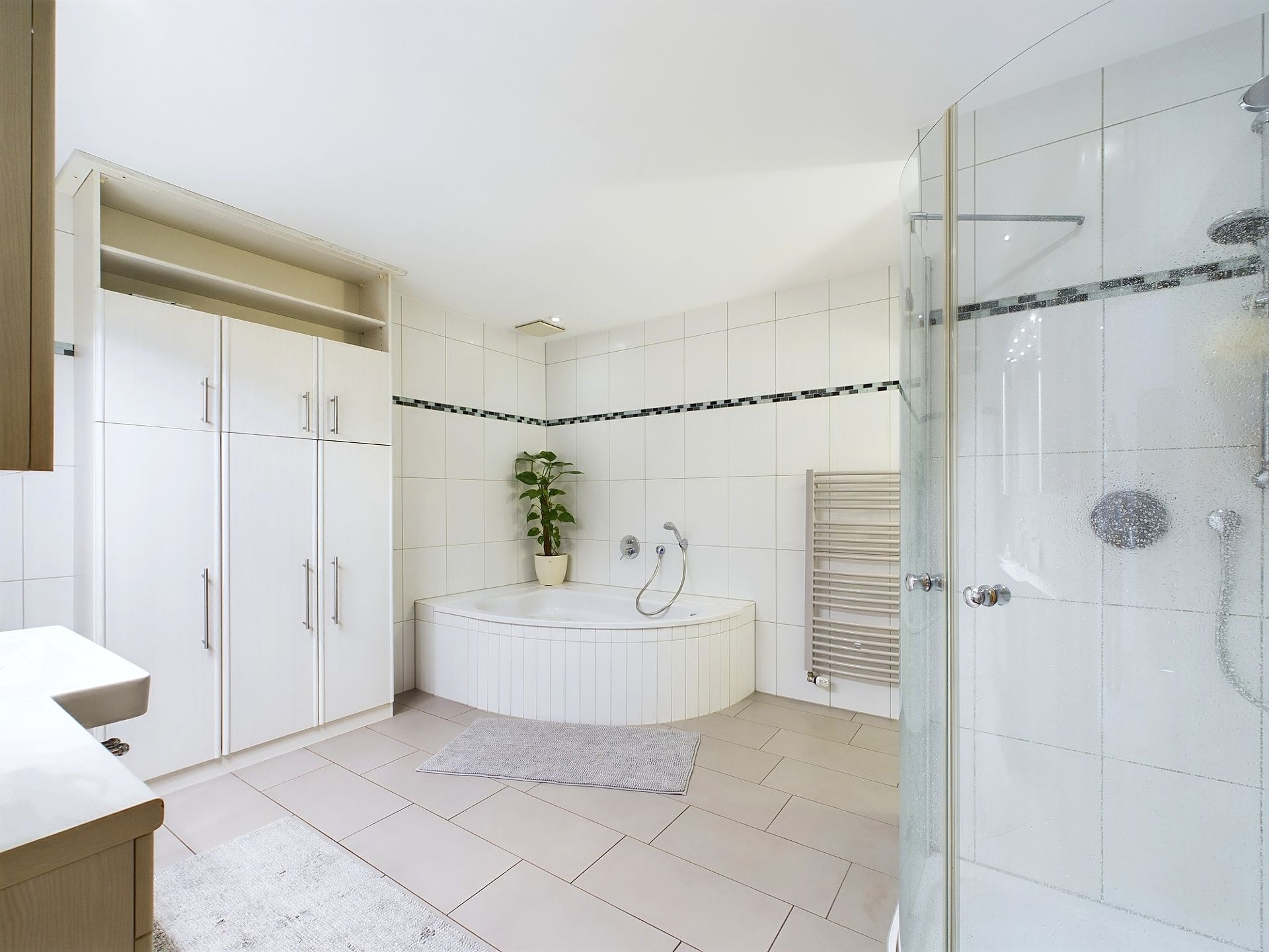 Modernes Badezimmer mit runder Badewanne, Duschkabine, weißen Schränken und einer Pflanze.