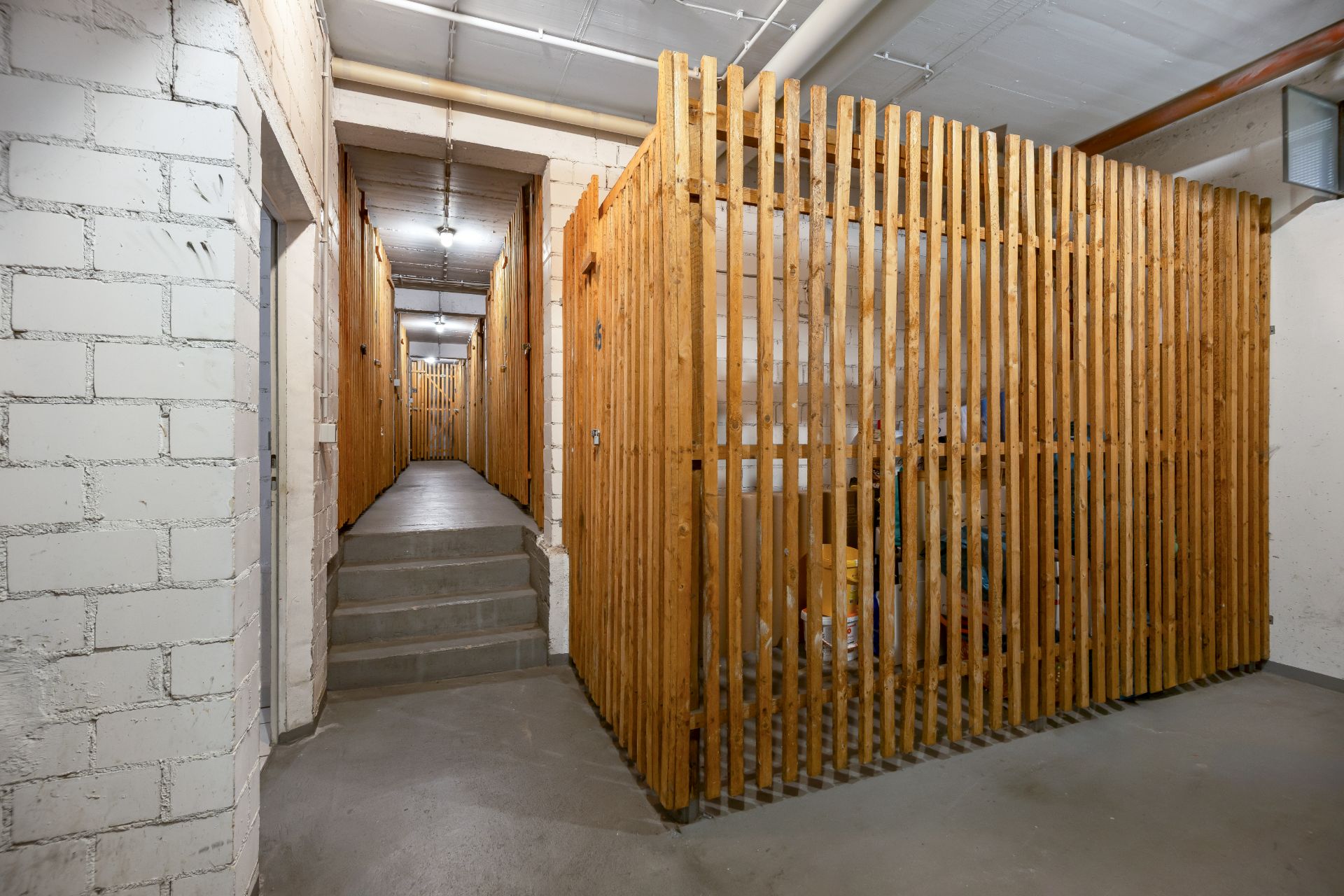 Gang mit mehreren Kellerabteilen aus Holzlatten und Betonwänden.