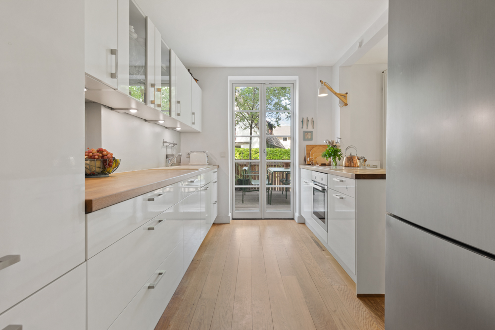Moderne, helle Küche mit weißen Schränken, Holzboden und Glastür zum Garten.
