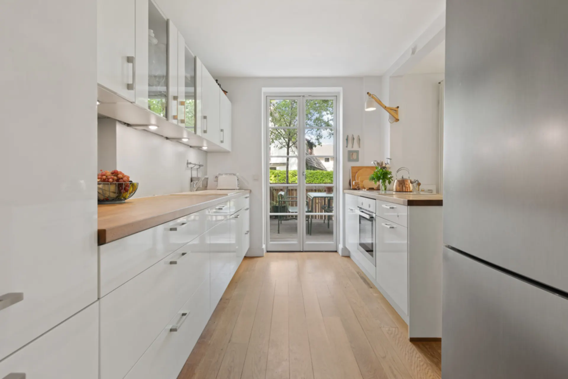 Moderne, helle Küche mit weißen Schränken, Holzboden und Glastür zum Garten.