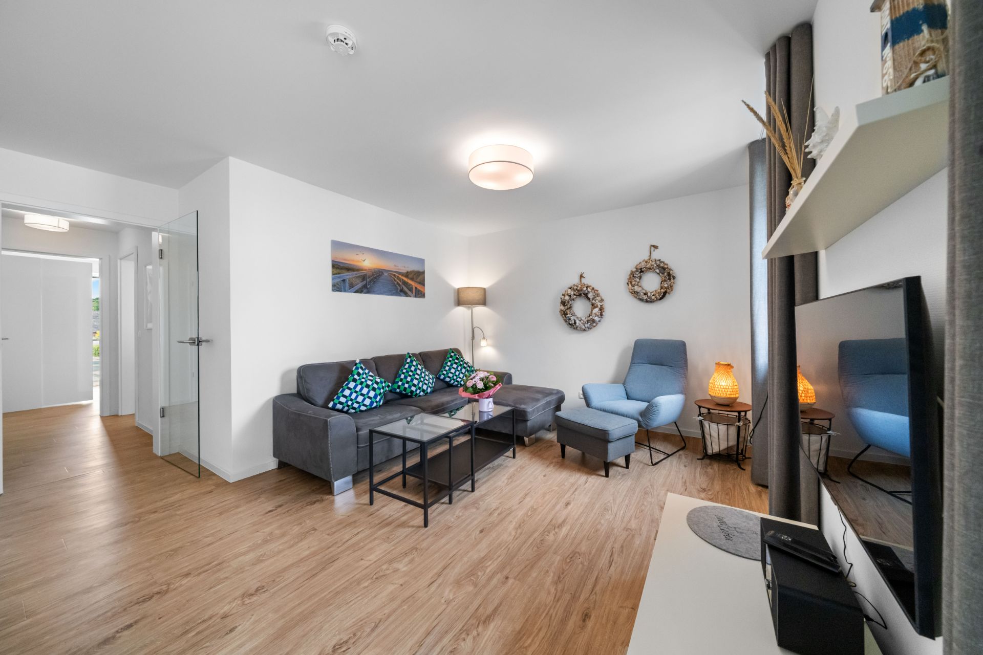 Modernes Wohnzimmer mit grauem Sofa, blauem Sessel, Holzboden und Fernseher.