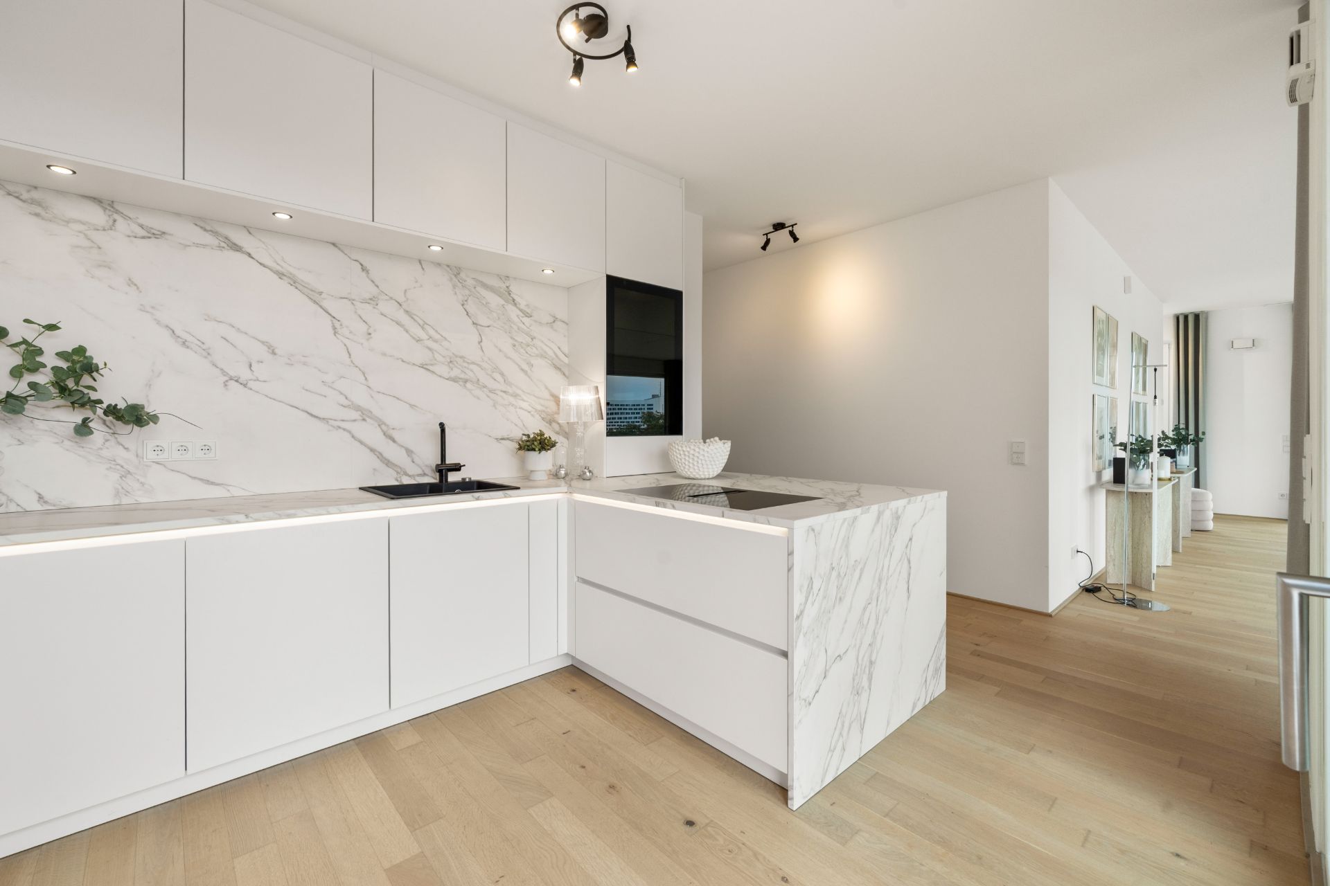 Moderne weiße Küche mit Marmorarbeitsplatten und Holzfußboden, Pflanzen als Dekoration.