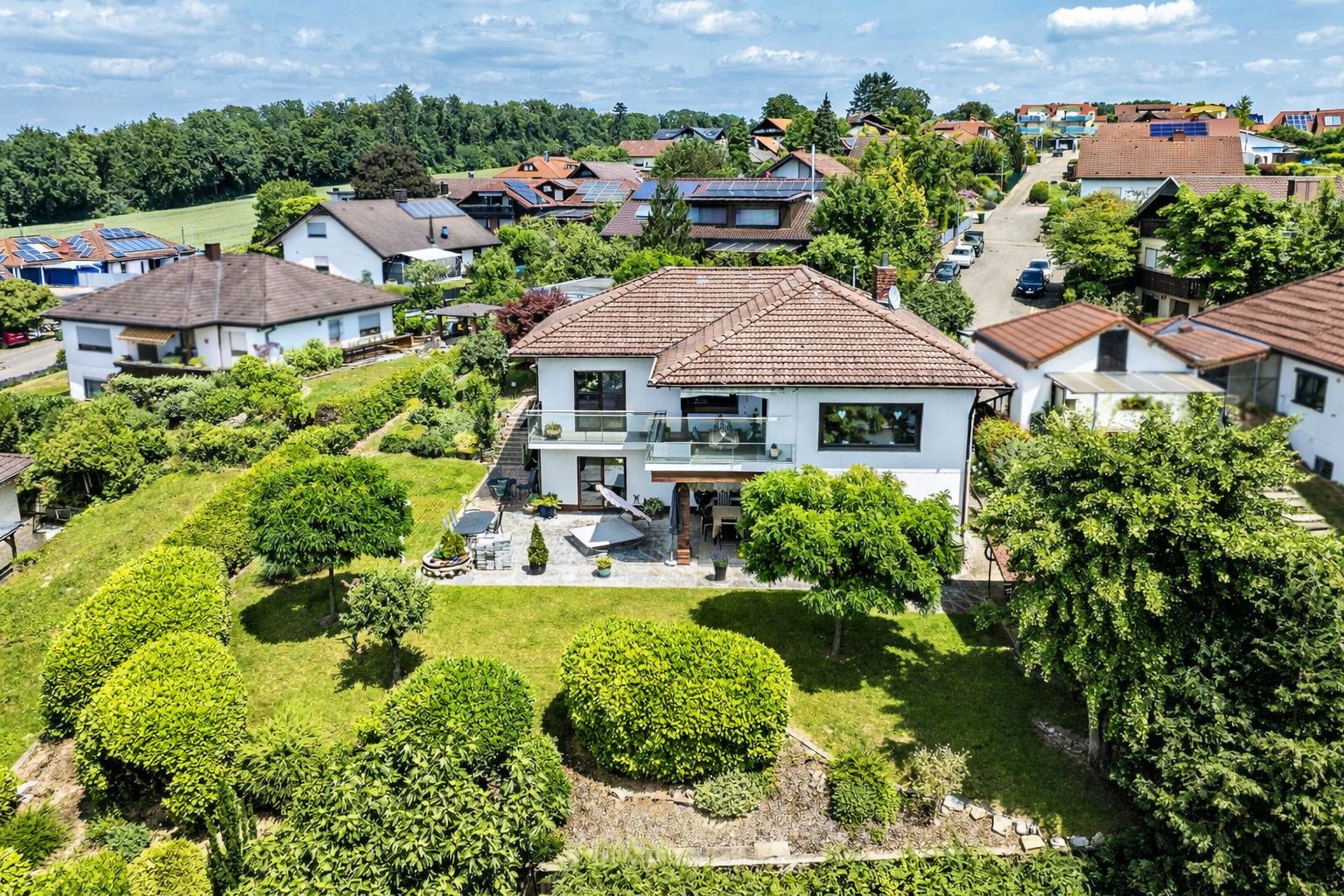 Luftaufnahme eines weißen Einfamilienhauses mit großem Garten und Terrasse in einer Wohnsiedlung.