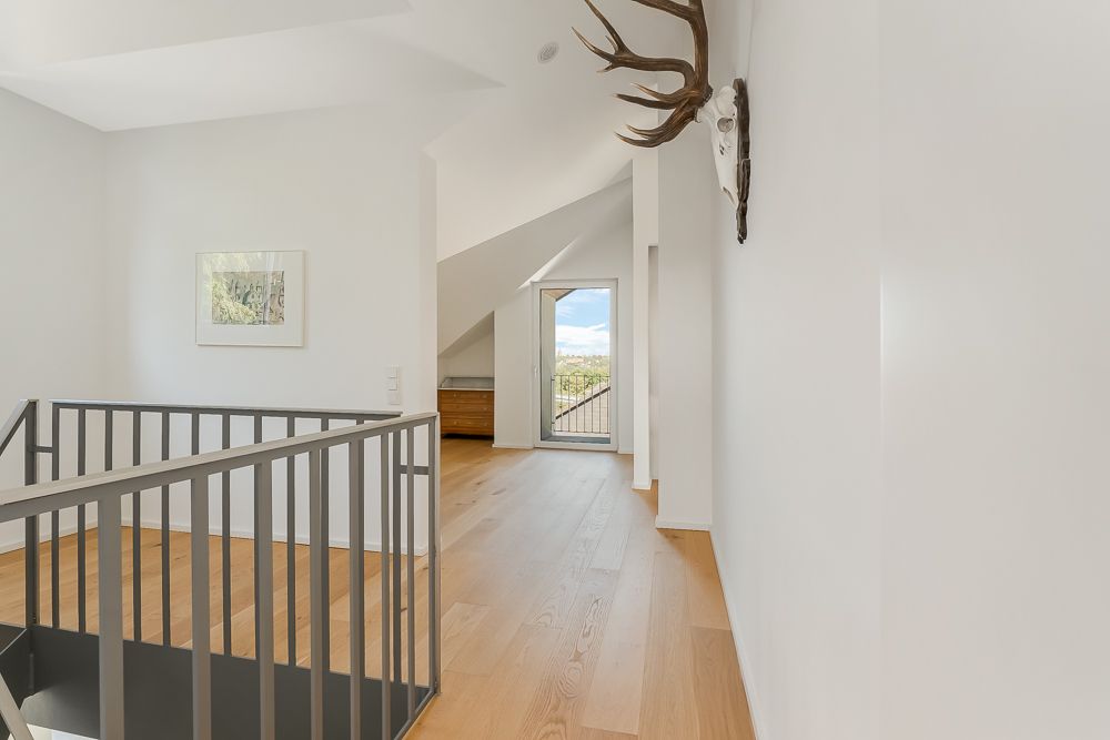 Heller Flur mit Holzfußboden, Treppengeländer, Geweih an der Wand und Zugang zu einem Balkon.