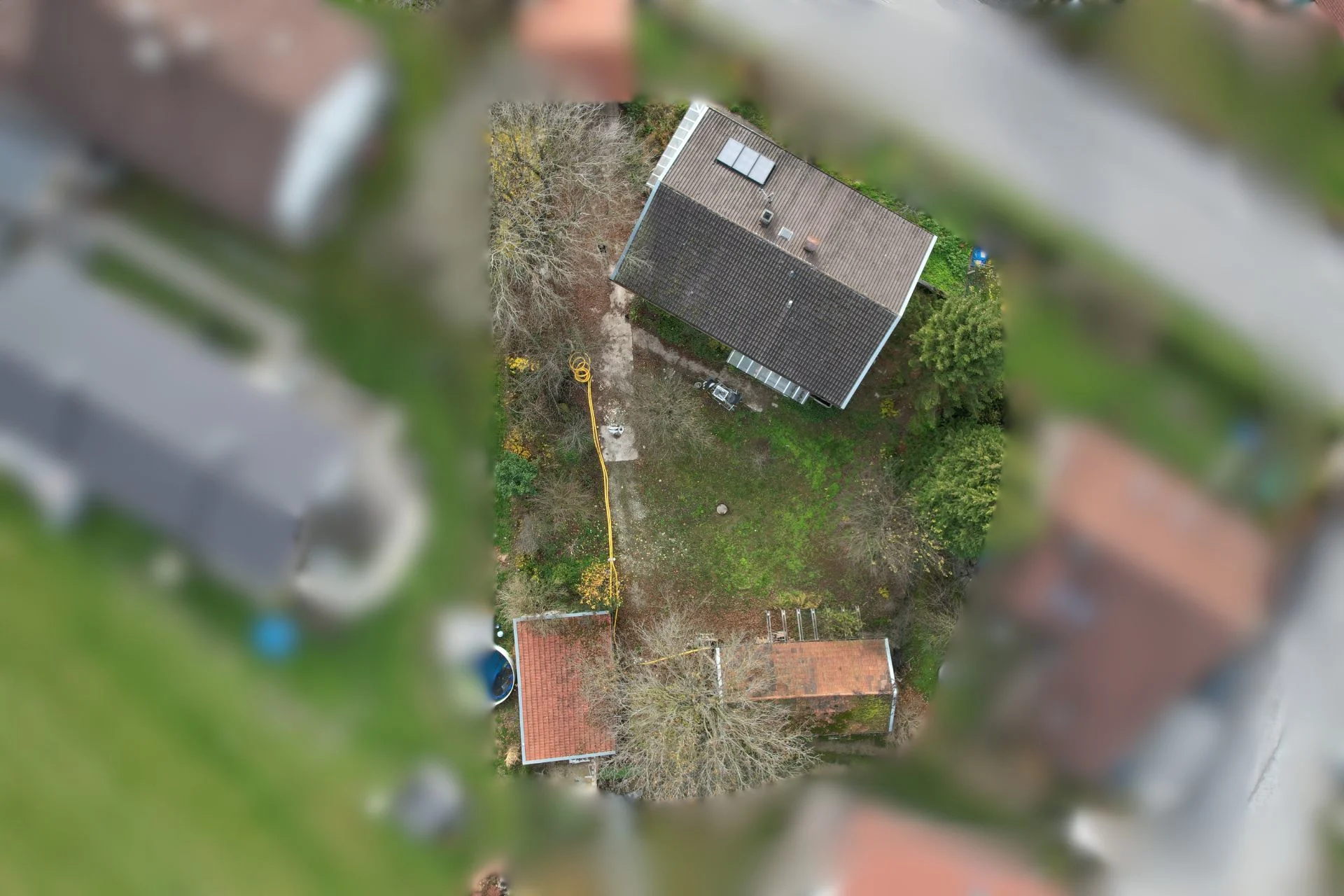 Luftaufnahme eines Hauses mit Garten und Nebengebäude, umgeben von Bäumen.