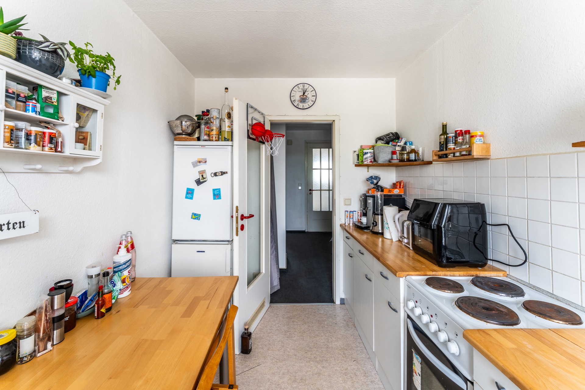 Helle Küche mit Holzarbeitsplatten, Elektroherd, Kühlschrank, Regalen und Gewürzen.