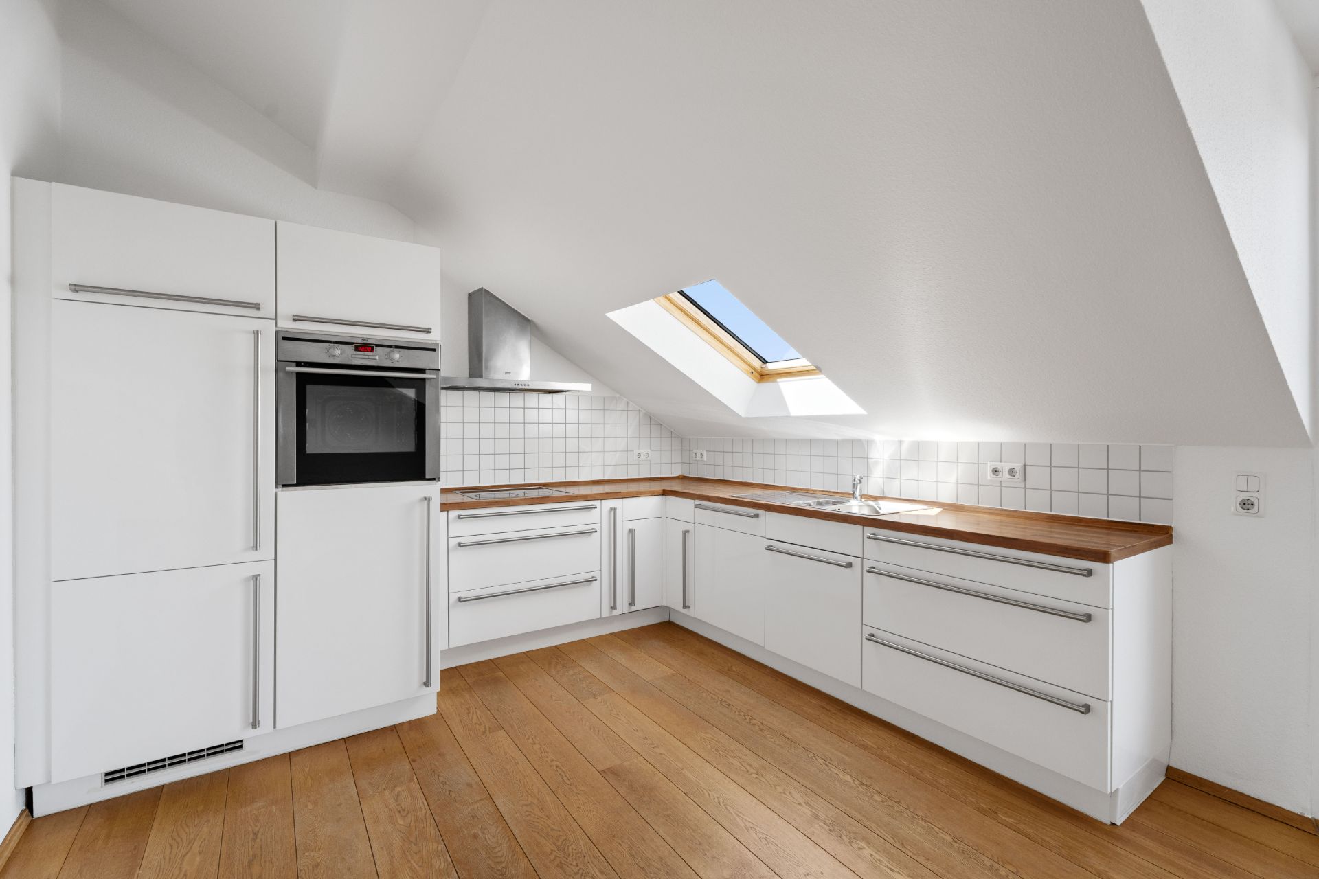 Moderne weiße Küche mit Holzarbeitsplatte und Dachfenster unter einer Dachschräge.