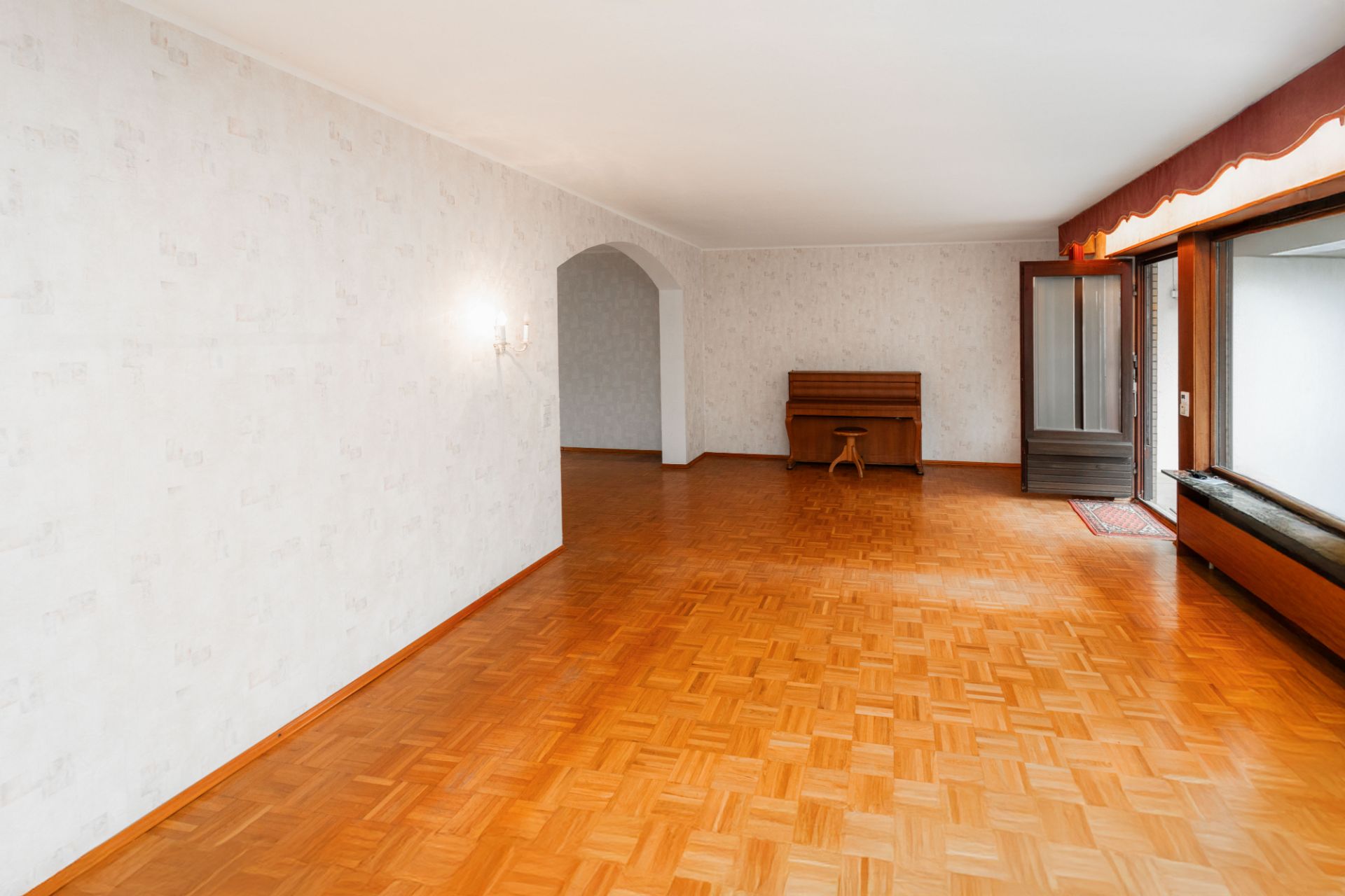 Helles Wohnzimmer mit Parkettboden, einem Klavier und einer offenen Glastür zum Außenbereich.
